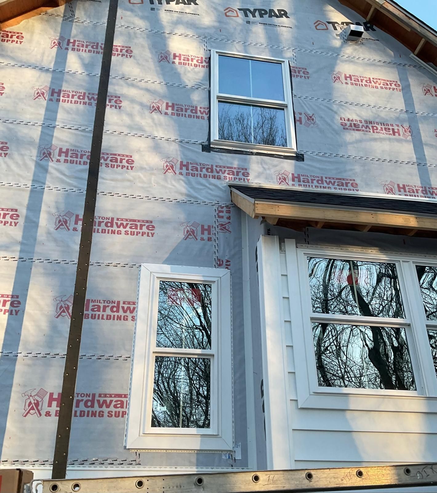 Exterior wall of a house under construction with Typar house wrap, two installed windows, and a partially sided alcove.