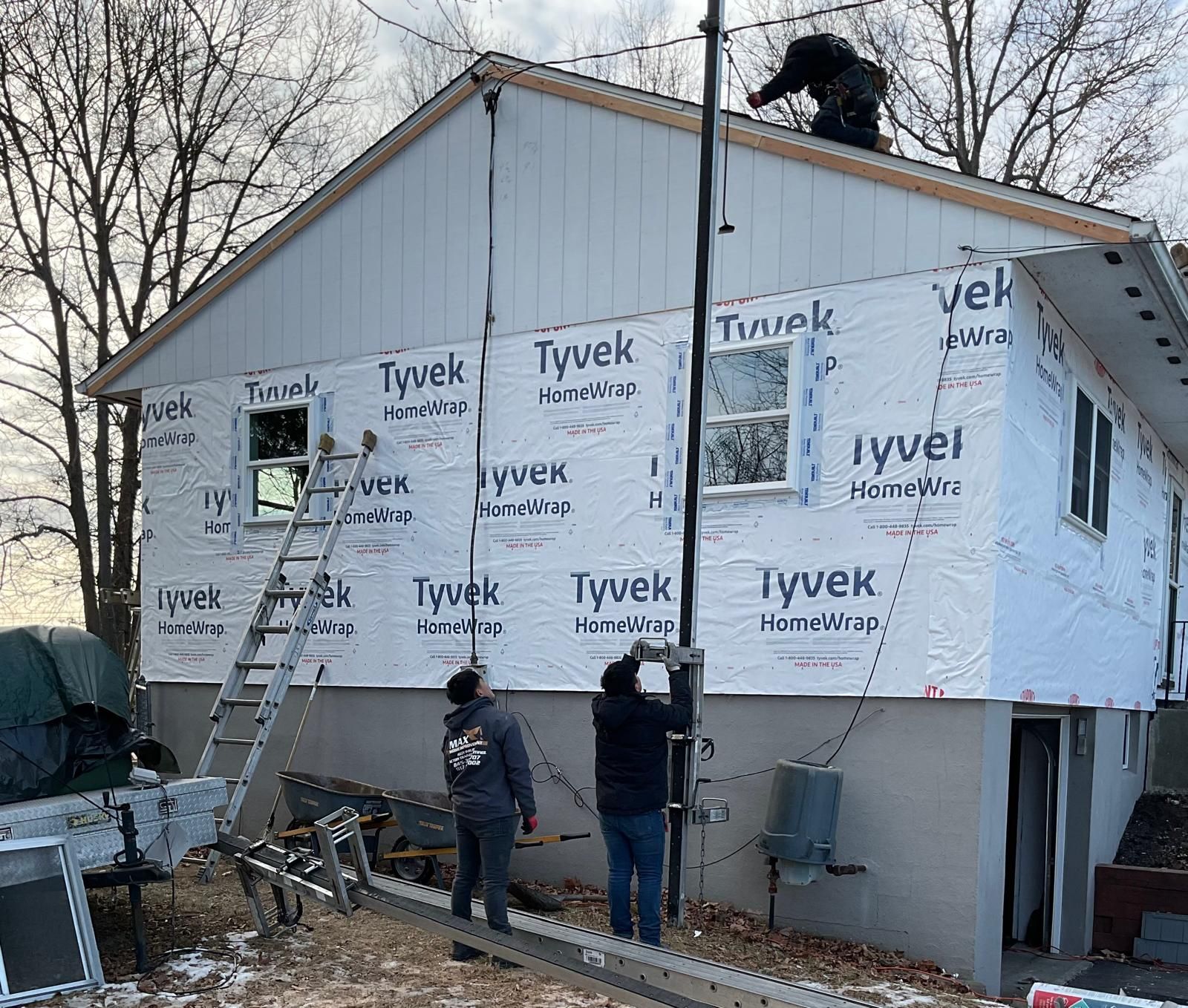 Three construction workers work on the exterior of a two-story house under renovation, covered in Tyvek house wrap.
