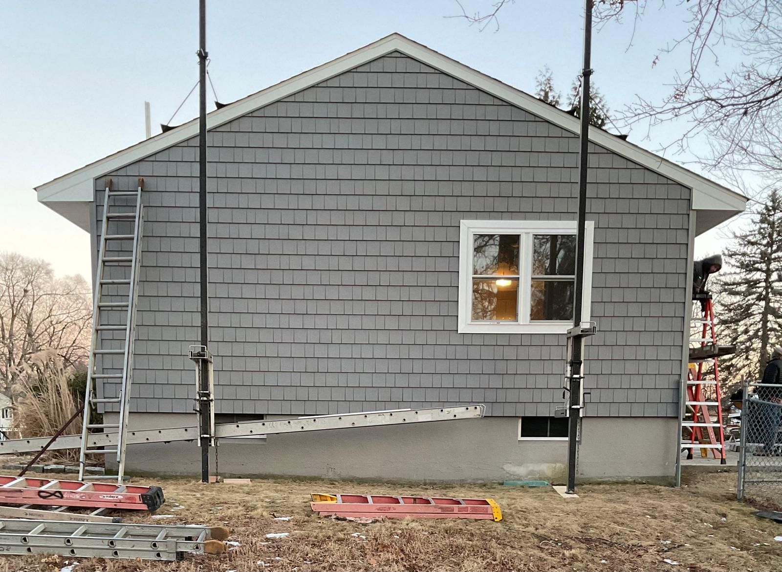 A grey-sided house exterior under renovation with scaffolding and ladders present in the yard.
