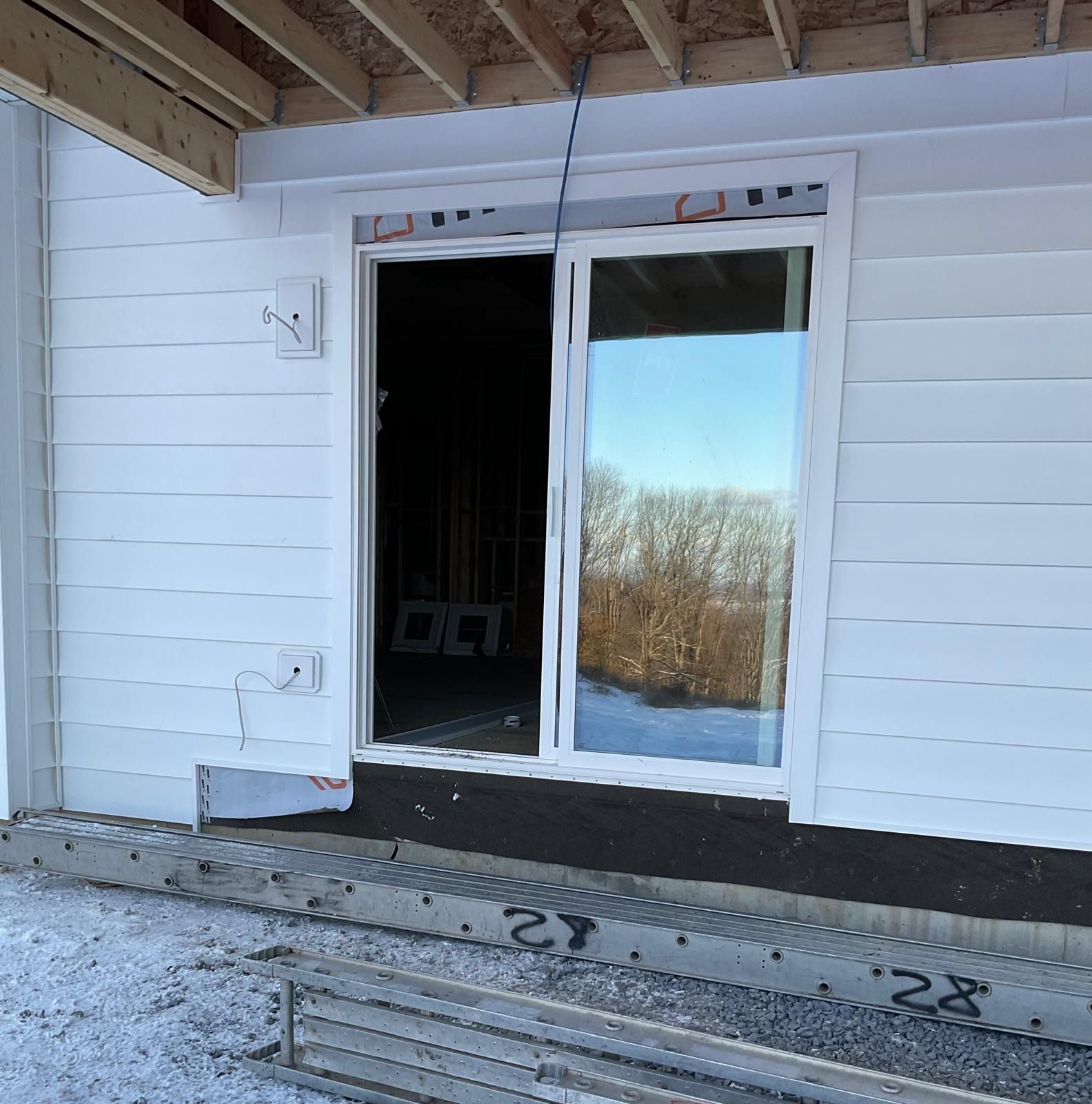 A sliding glass door installed in the unfinished exterior wall of a white-sided house under construction.