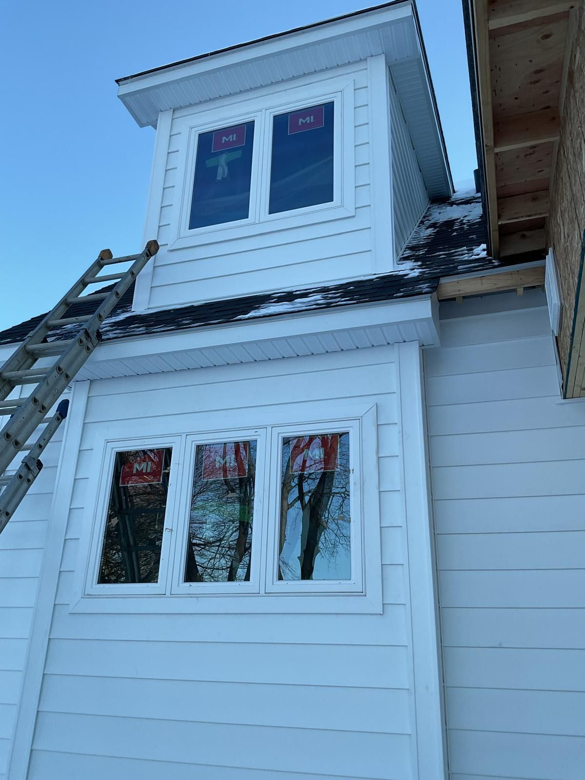 An outdoor view of a white, multi-level house addition featuring new windows, siding, and a ladder leaning against a wall.