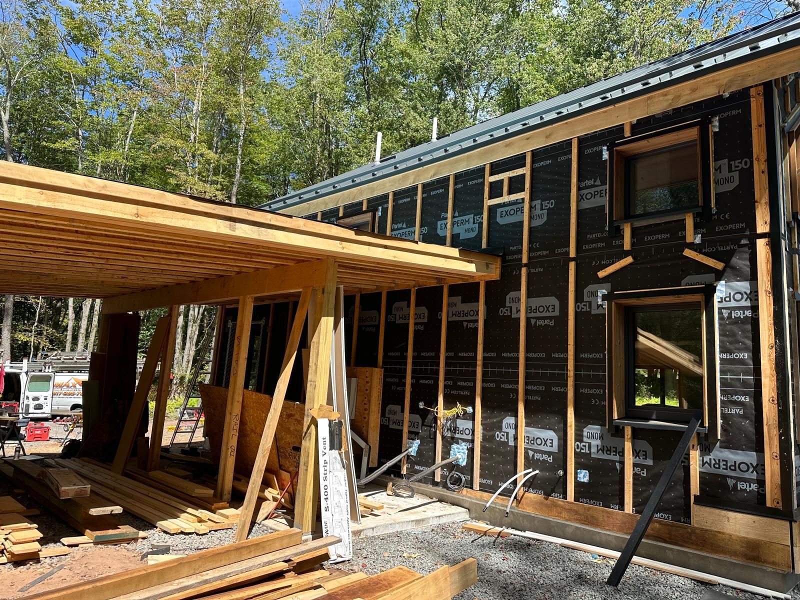 Exterior of a house under construction with a wooden porch frame and black weather-resistant building wrap on the walls.
