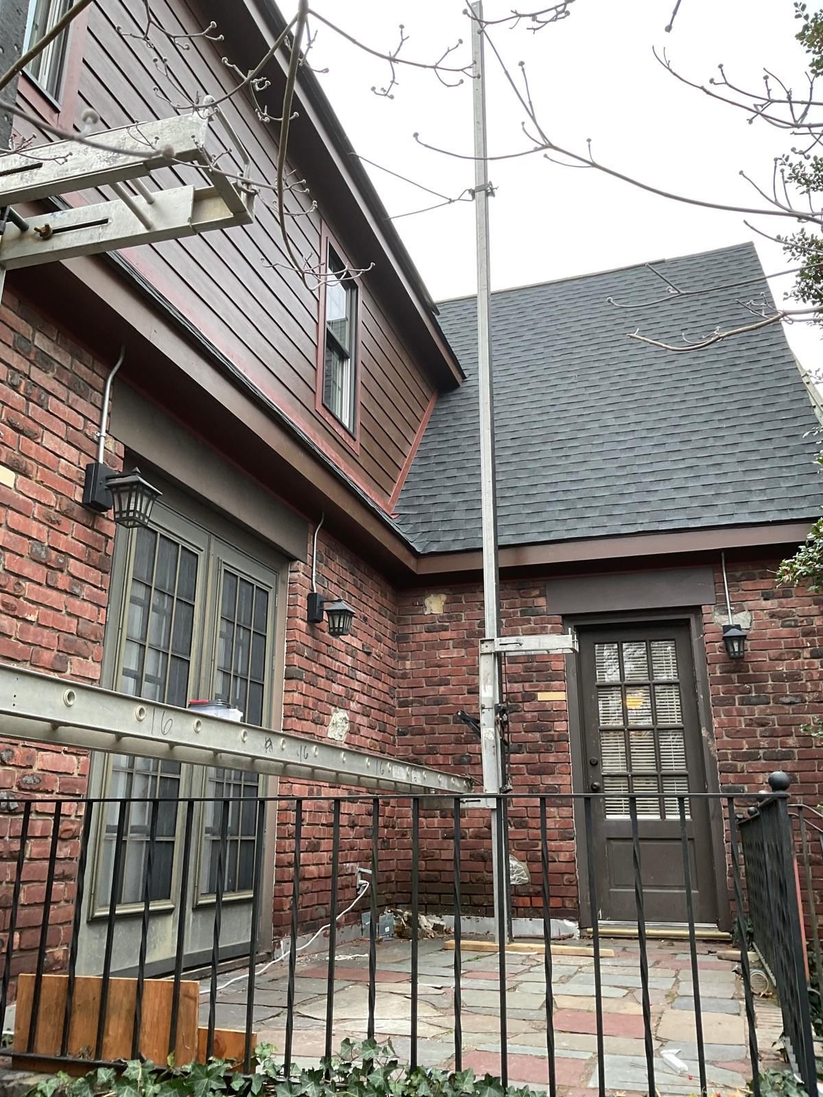 A brick patio area with French doors, a wooden door, and a tall metal pole extending upward.