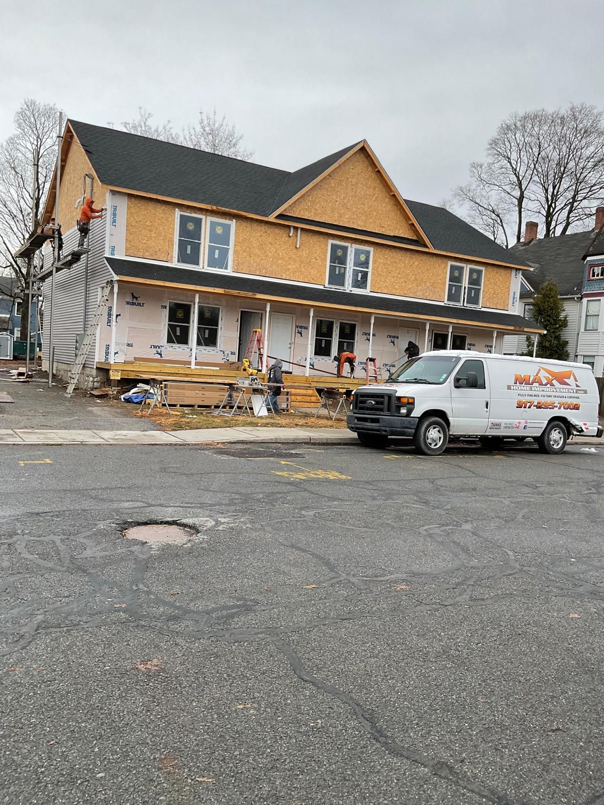 A two-story building under construction with yellow siding, a new roof, and a white service van parked in front.