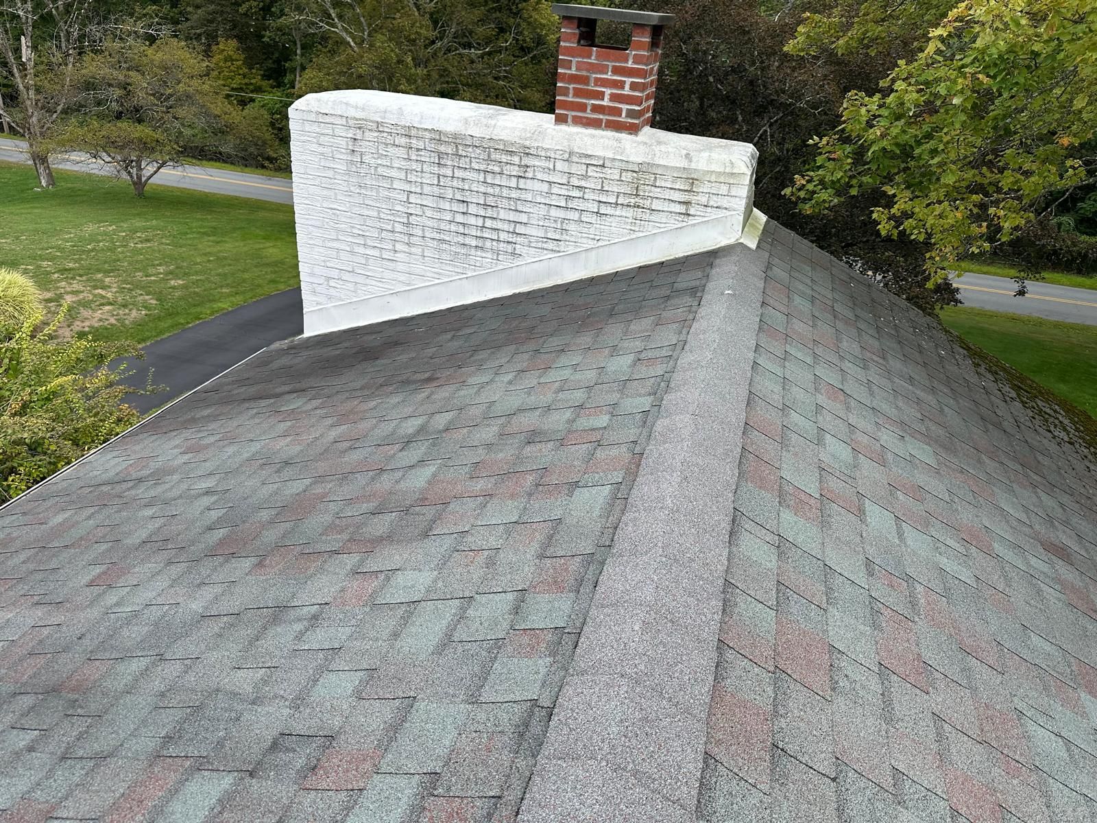 A high-angle view of a gray shingled roof featuring a large, white-painted brick chimney stack with a red brick top.