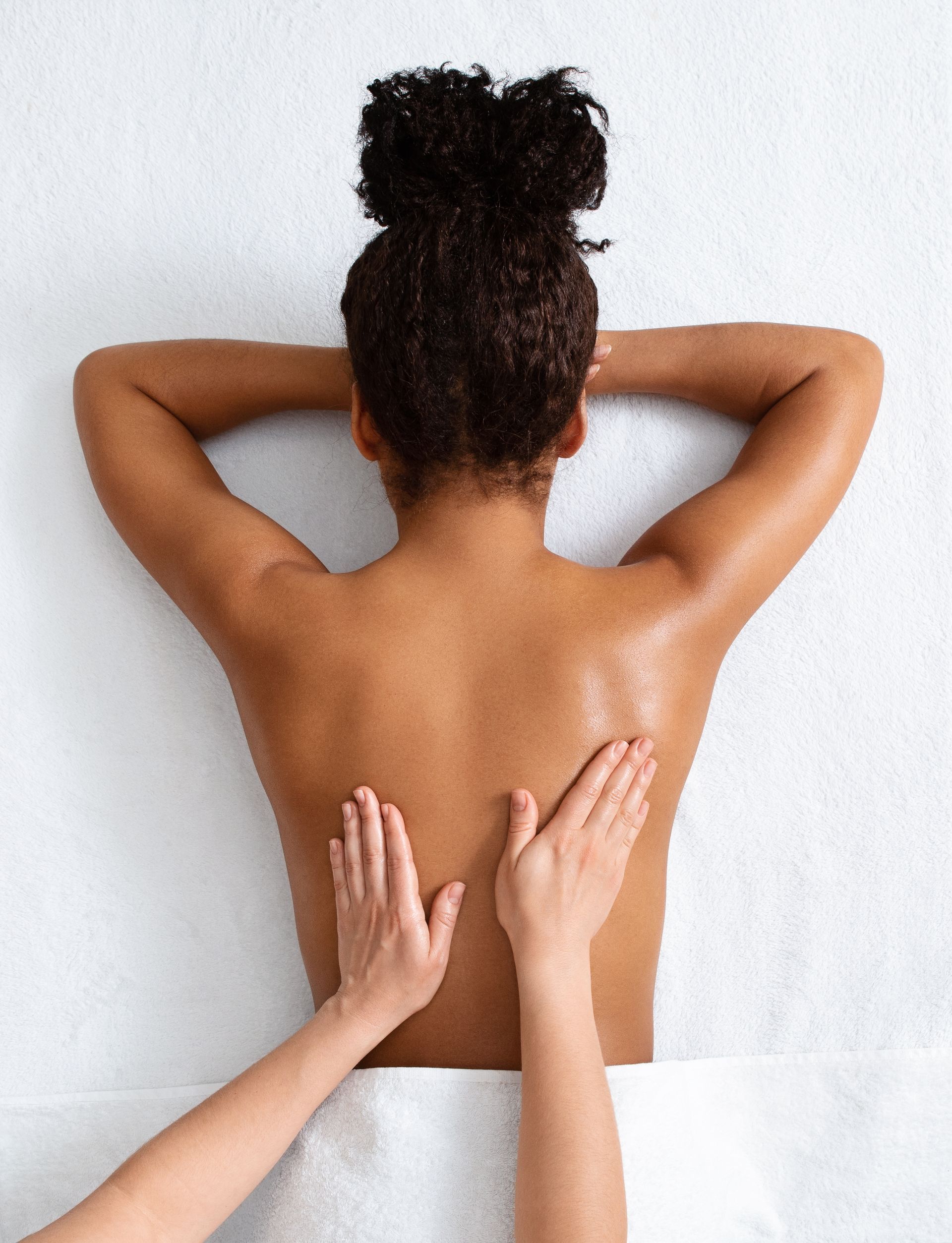 Person receiving a back massage on a white towel. Hands are massaging the back.