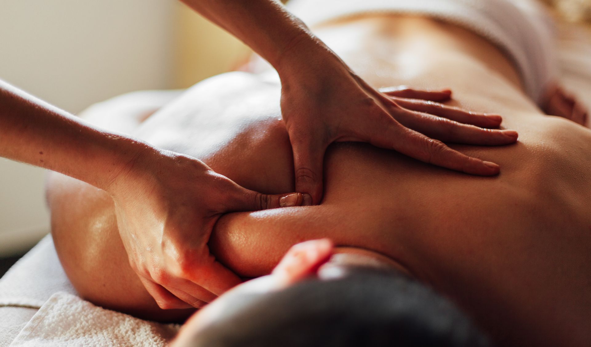 Hands massaging the back and shoulder of a person lying face down on a massage table.