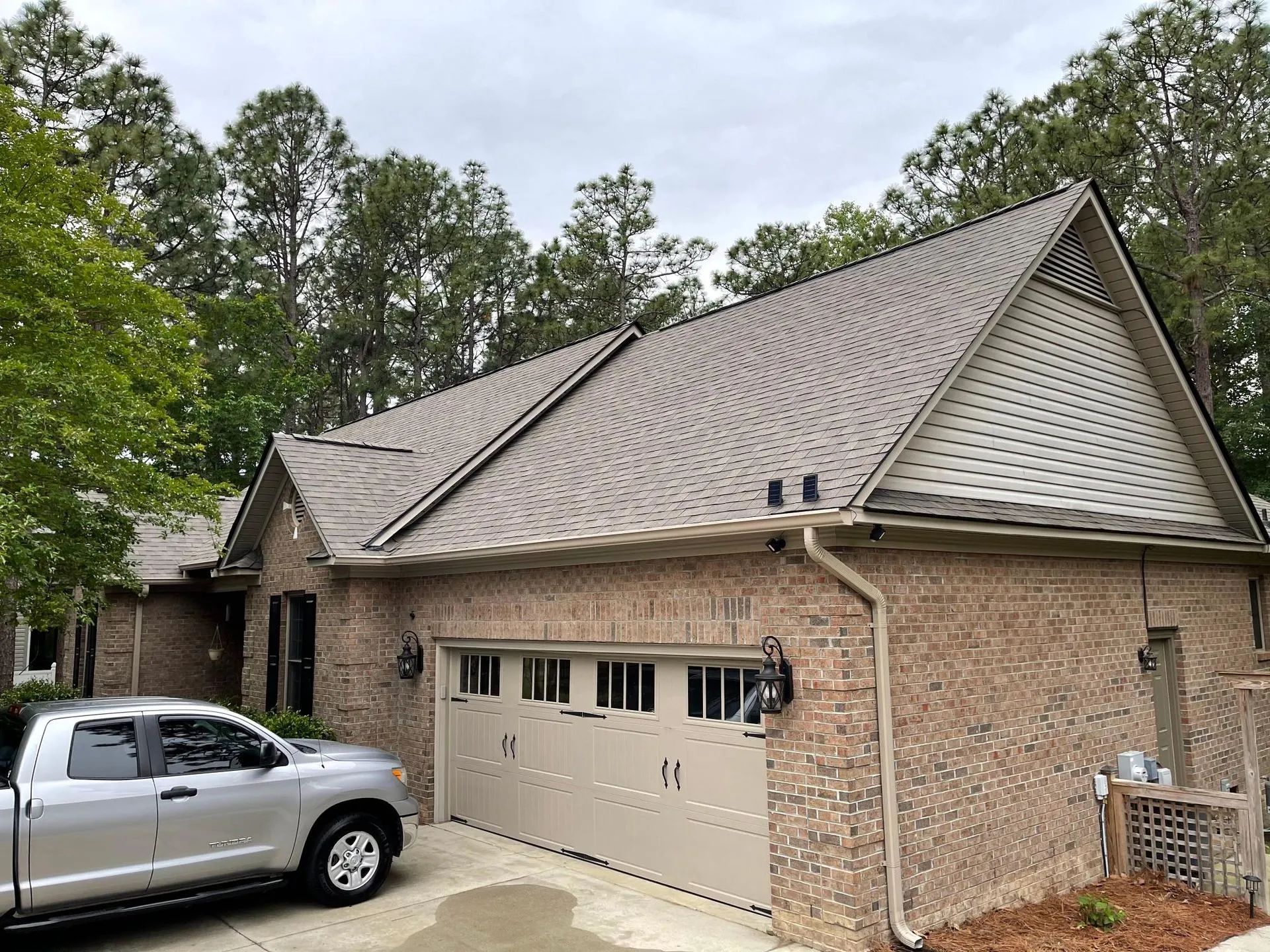 Brick house with a two-car garage, gray roof, and silver pickup truck parked outside