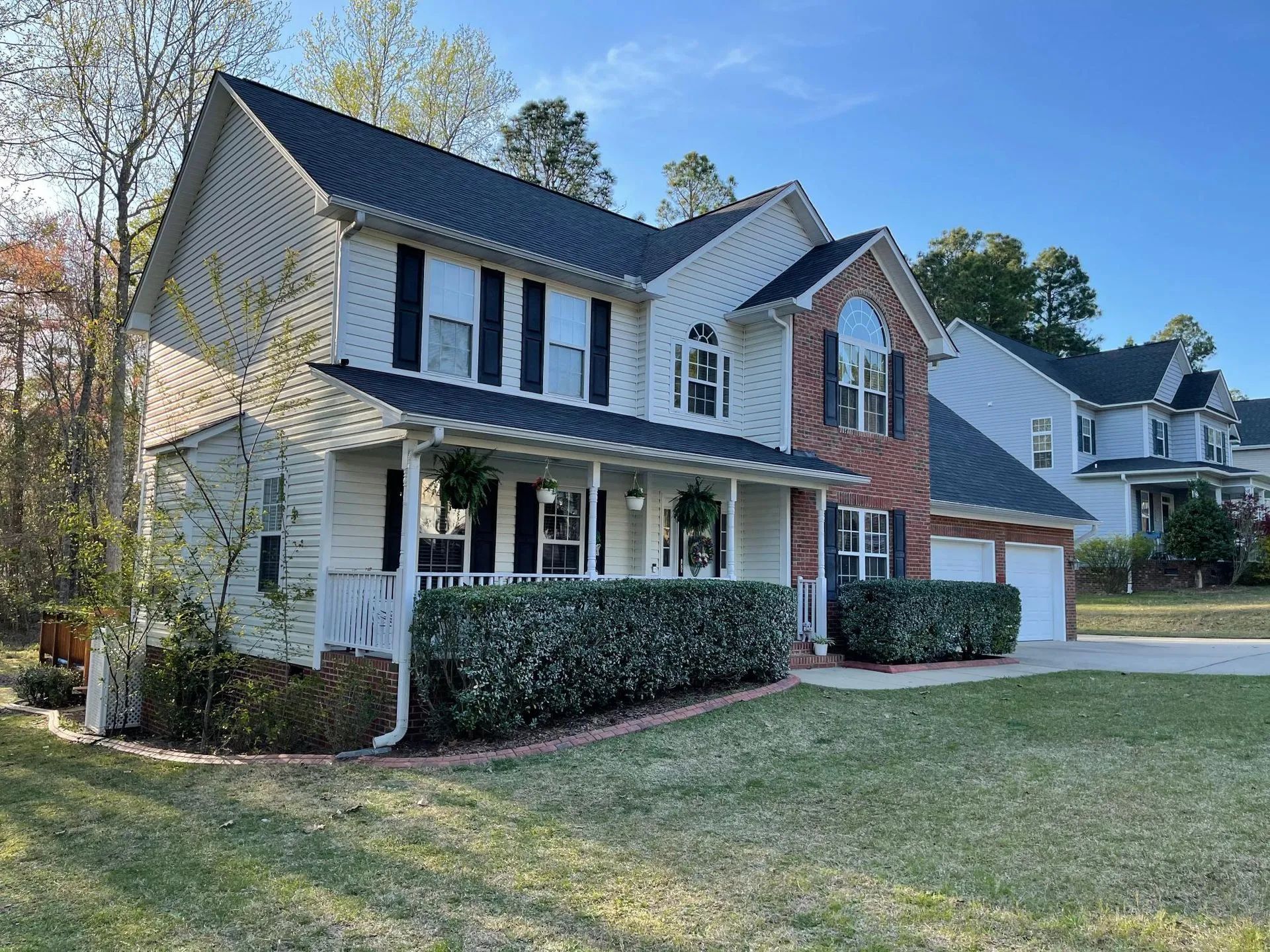 Suburban two-story house with white siding, brick accents, and a front porch on a sunny day