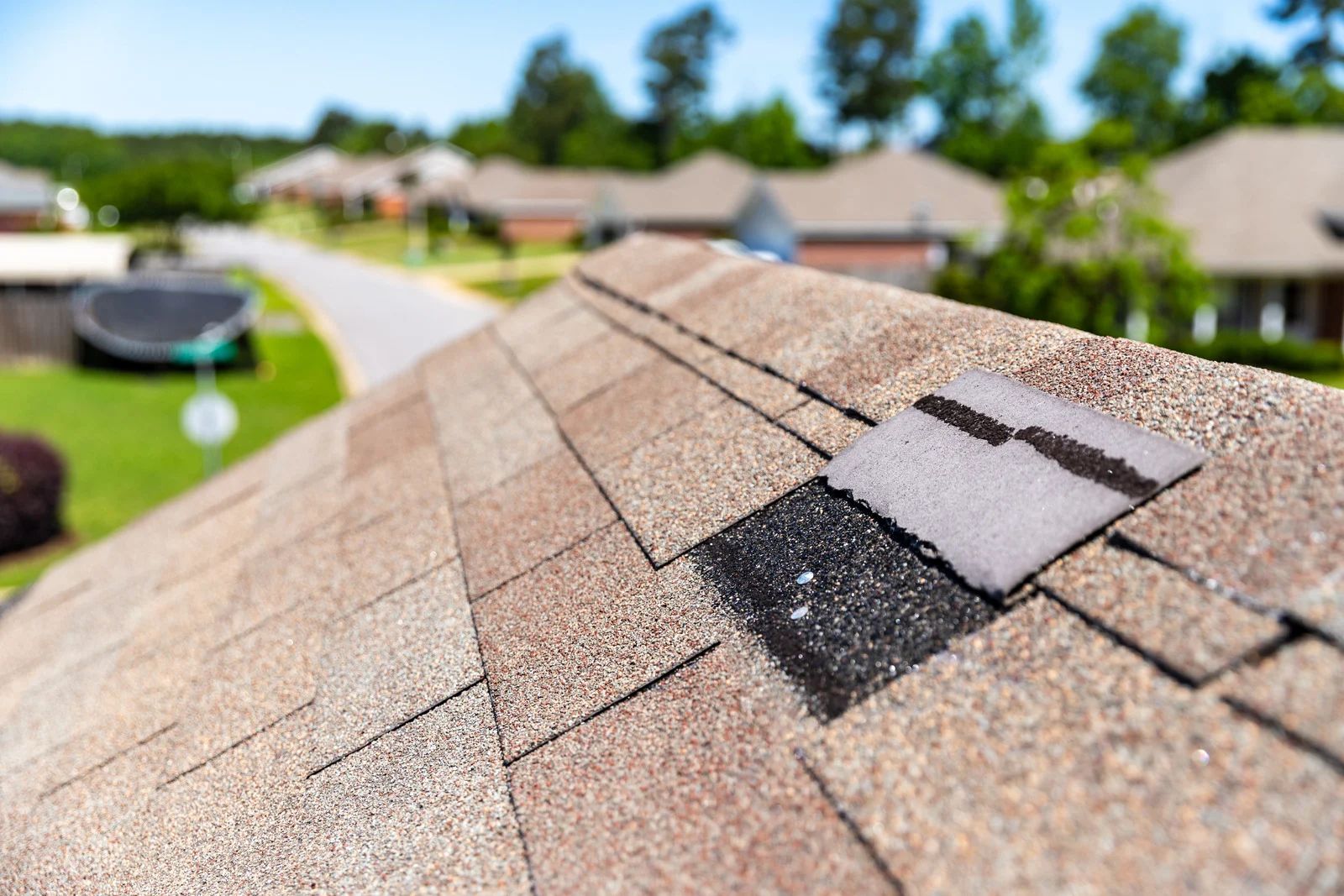 Damaged asphalt shingle roof with missing shingles; residential street in background.