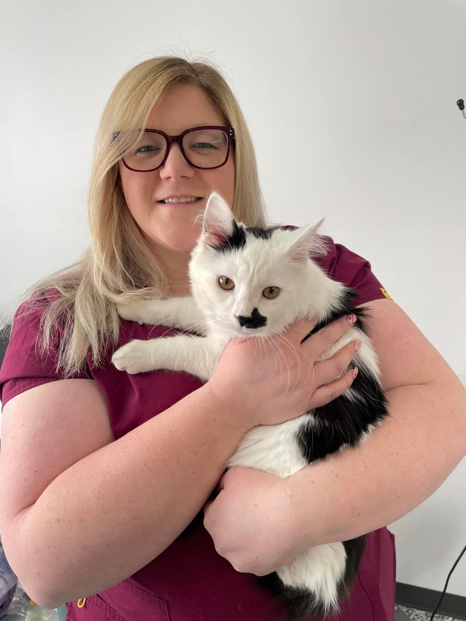 A woman is holding a black and white cat in her arms.