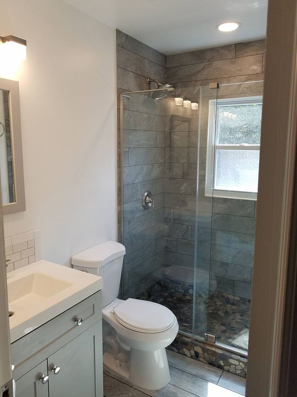 A bathroom featuring a light gray vanity, a white toilet, and a glass-enclosed shower with stone-look tile walls.