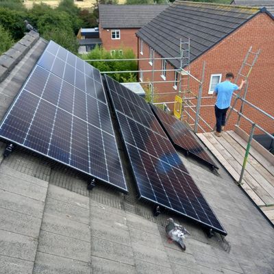 Bird-proofed solar panels installed on the roof of a building while a maintenance person walks by on scaffolding.