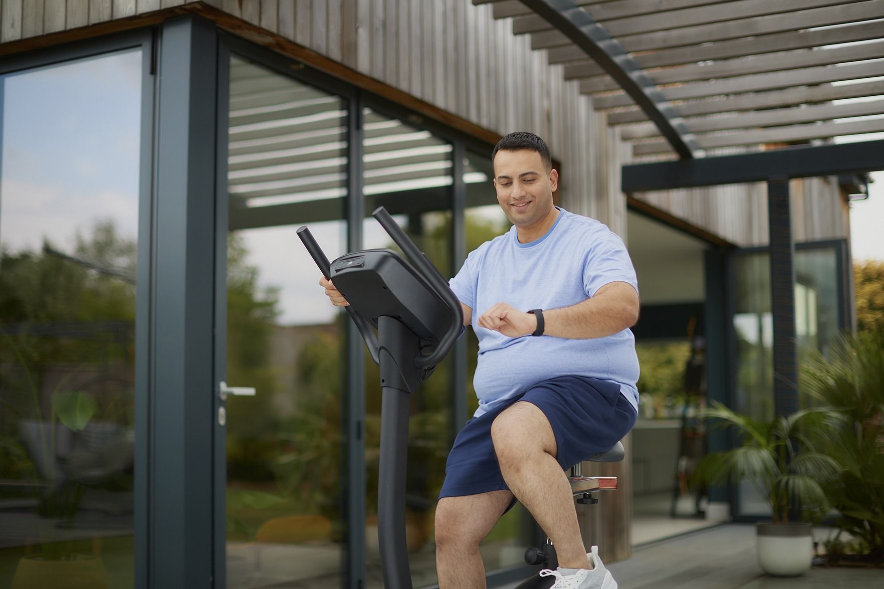 A man is riding an exercise bike outside of a house.
