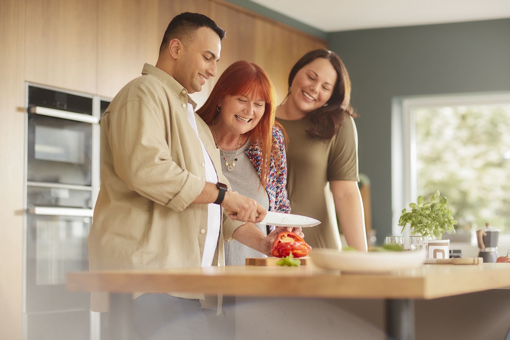 A man and two women are standing in a kitchen looking at a tablet.