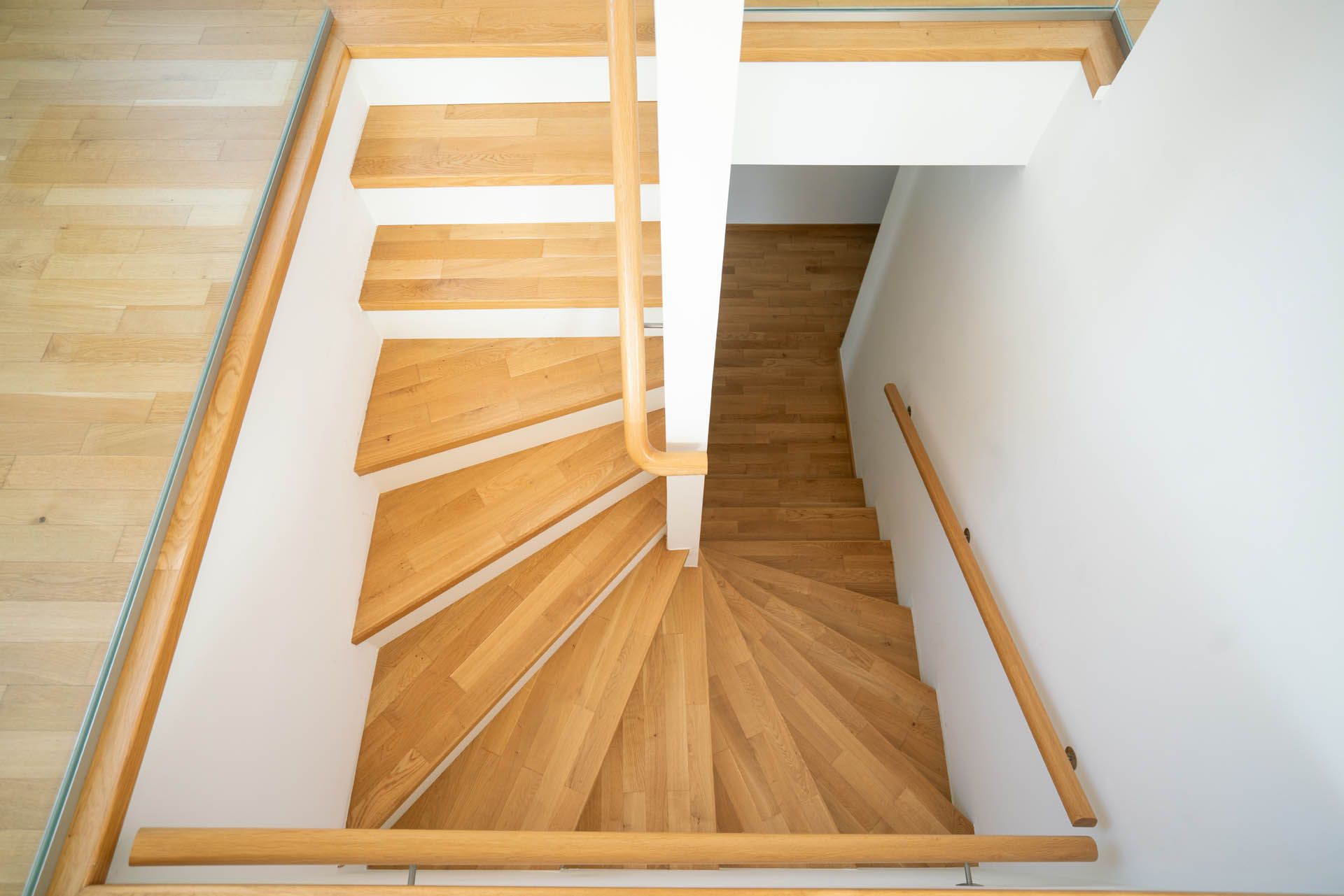 Holztreppe mit 180-Grad-Kurve, helles Holz, weiße Wände und ein Holzhandlauf.