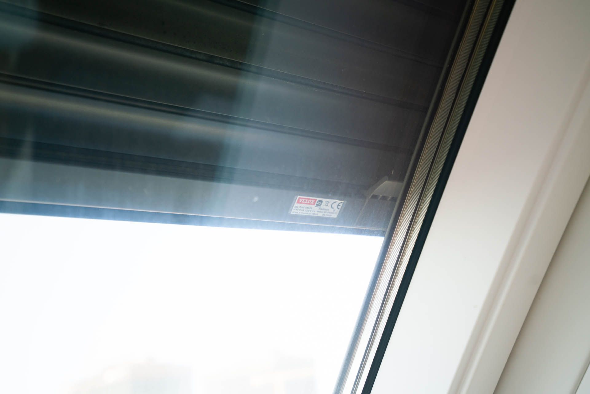 Nahaufnahme eines Fensters mit teilweise geschlossenem Fensterladen, weißem Rahmen und verschwommenem Blick nach draußen.