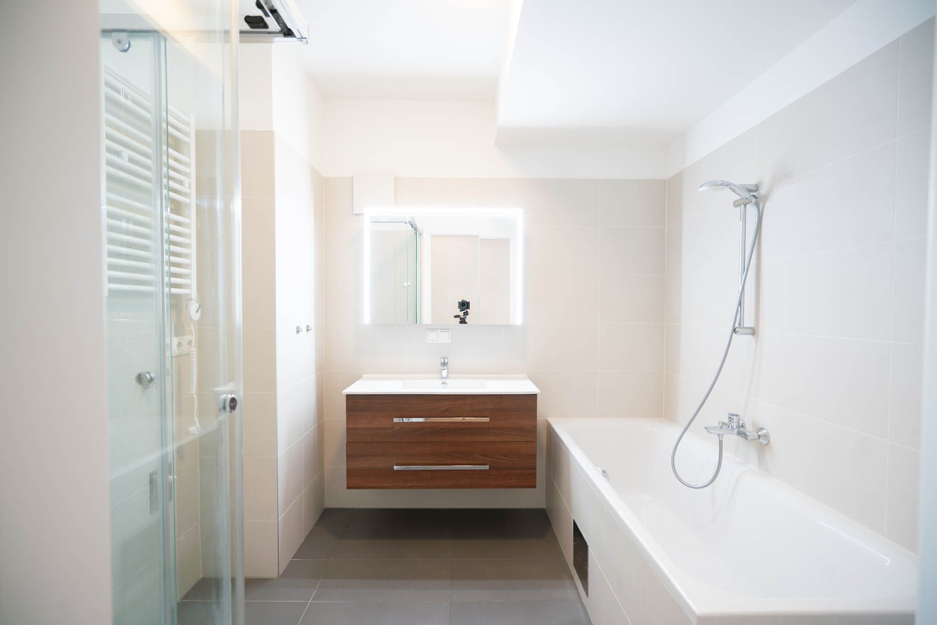 Modernes Badezimmer mit Glasdusche, Holzwaschtisch, Badewanne und Wänden und Boden in neutralen Farben.