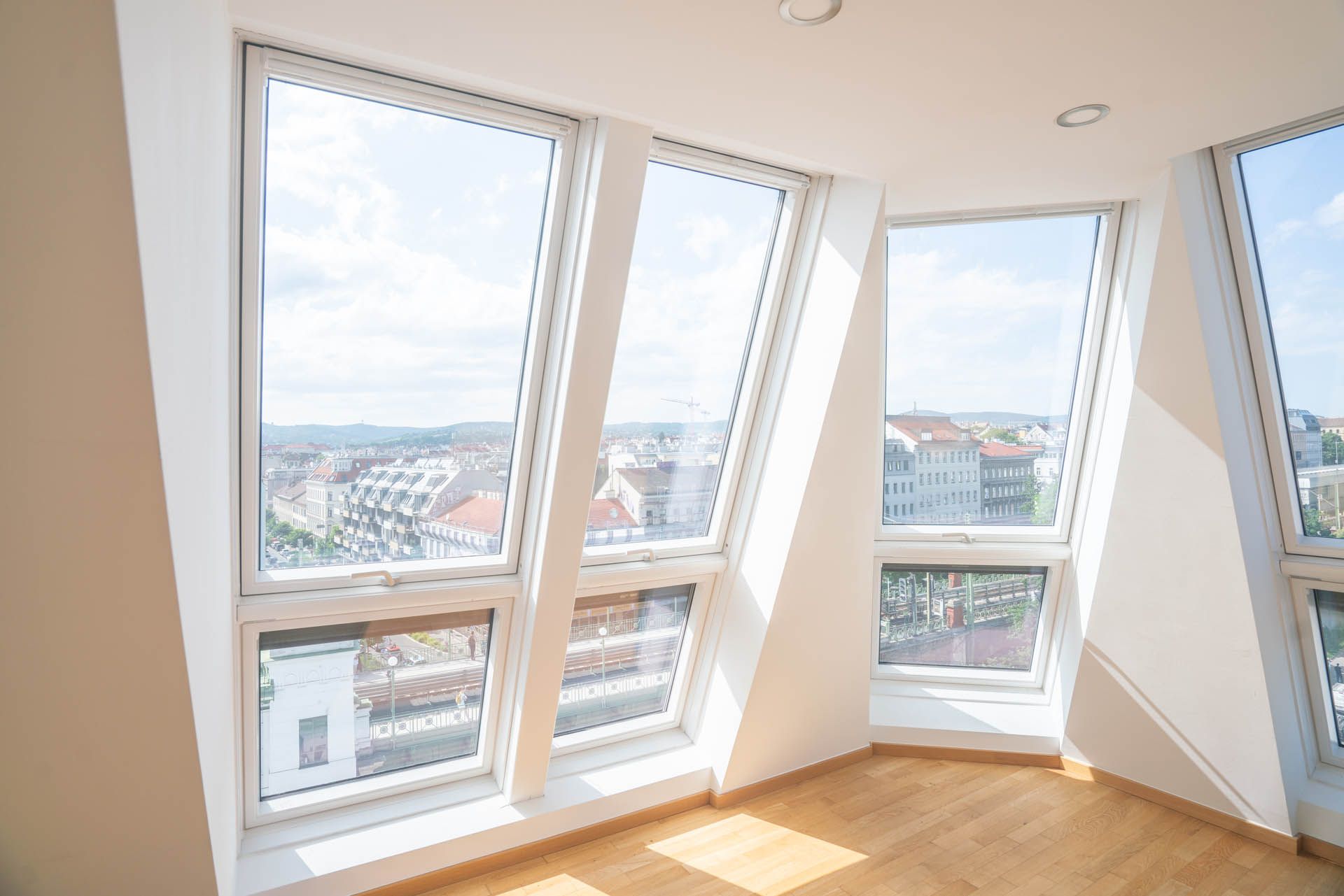 Heller Innenraum mit drei schrägen Fenstern mit Blick auf die Stadt, Hartholzböden.