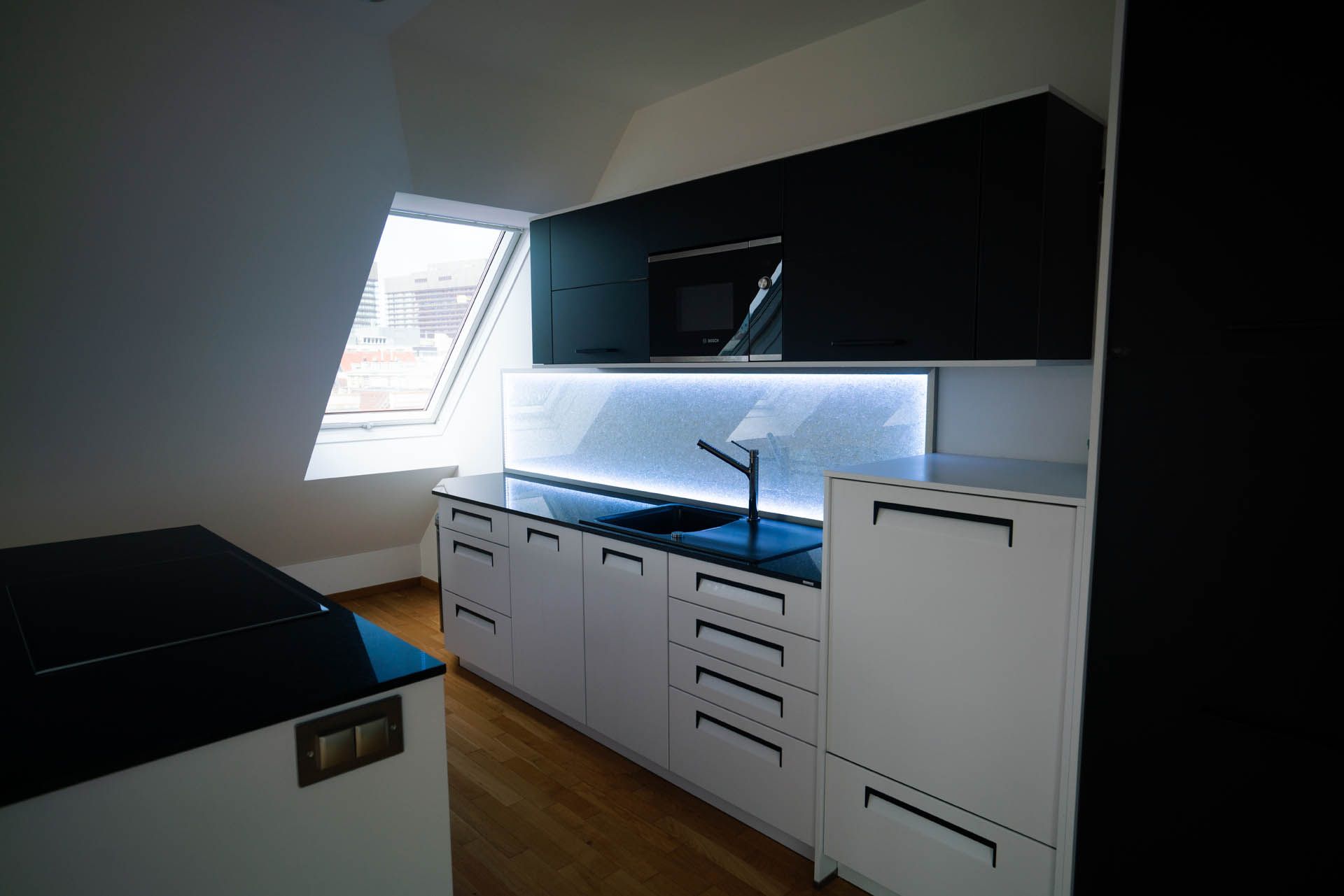 Moderne Küche mit weißen und schwarzen Schränken, eingebauter Mikrowelle und Oberlicht.