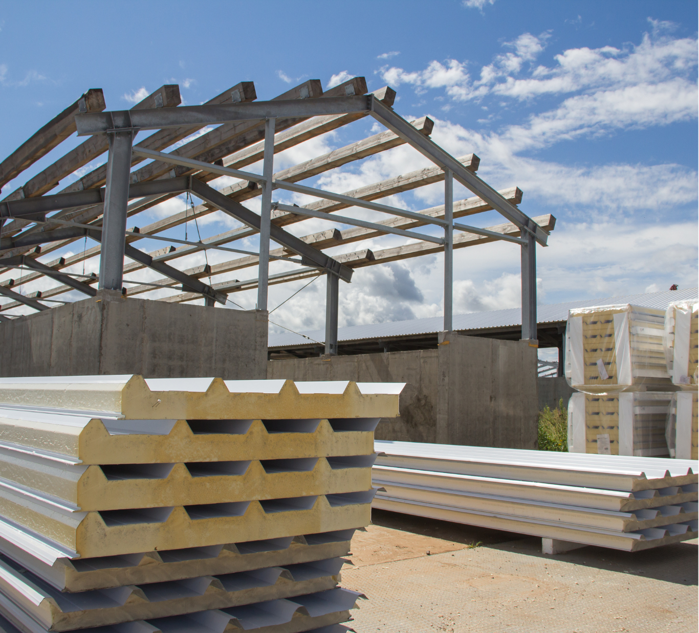 Stacks of insulated building panels in front of a steel-framed structure against a blue sky.