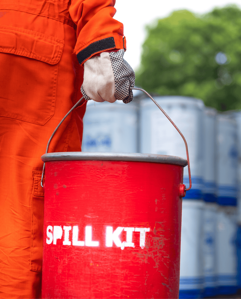 Person in orange suit holds a red spill kit bucket with 