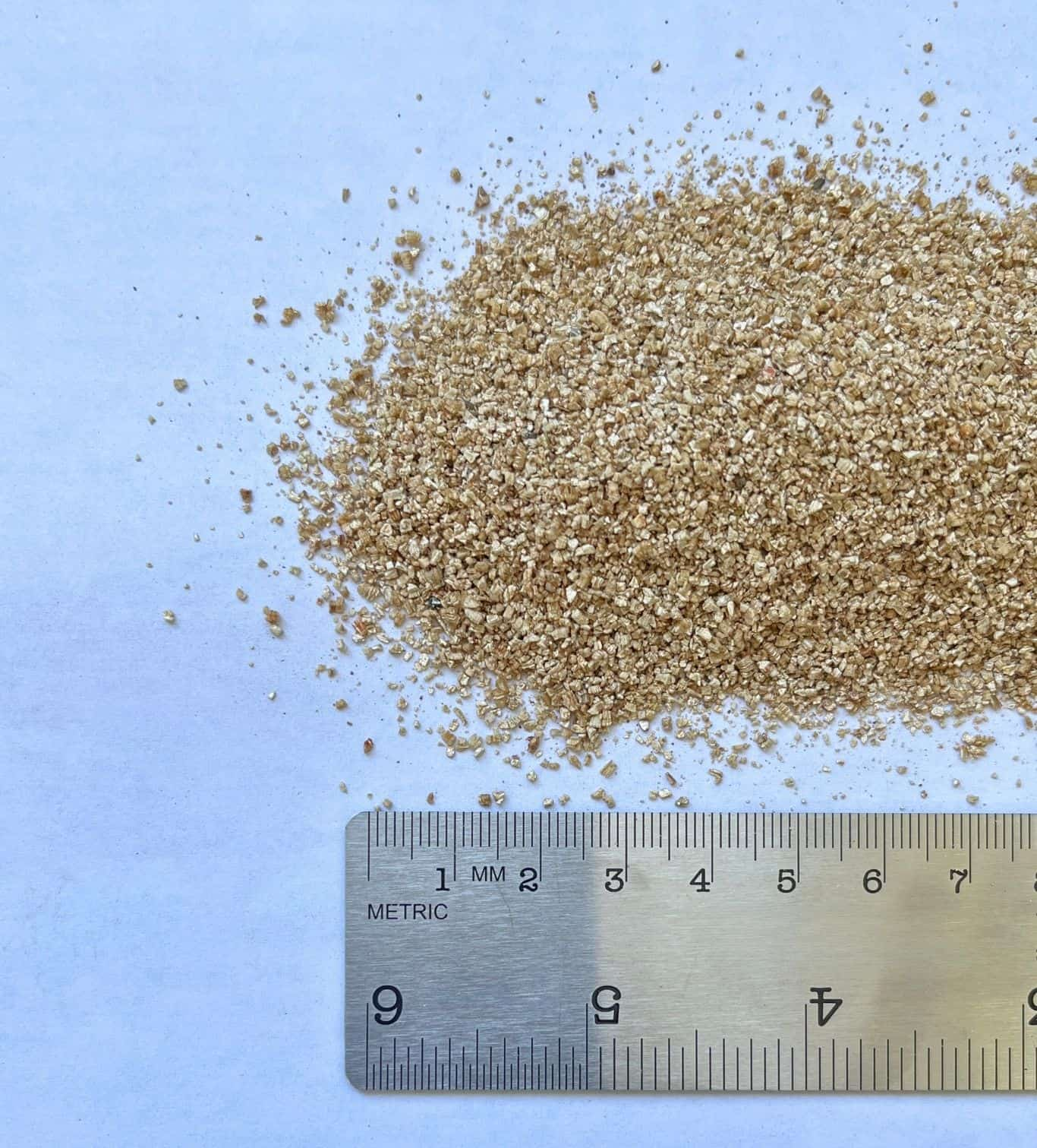 Pile of light brown, granular material next to a ruler showing metric measurements.