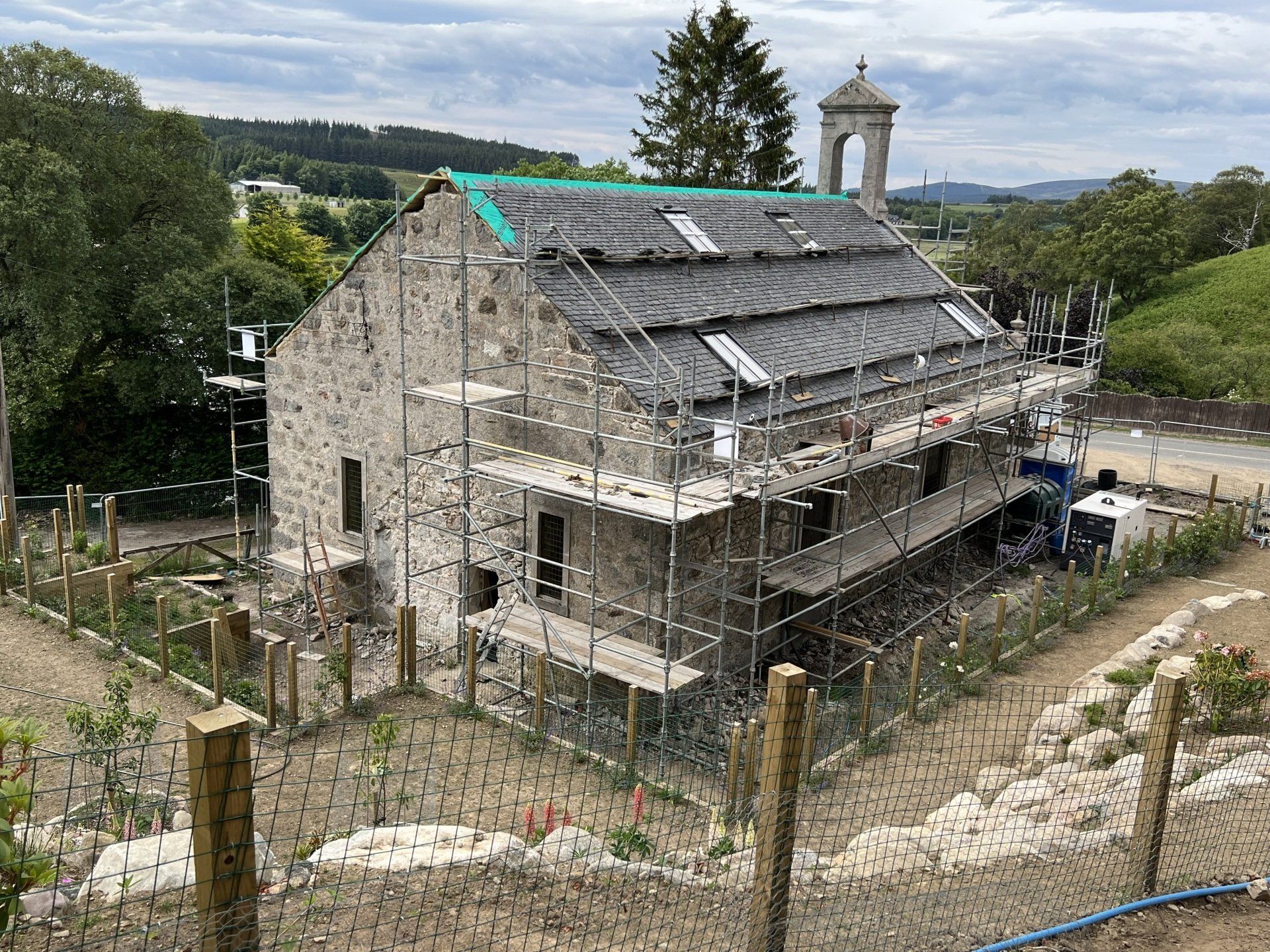 Stone barn under renovation with scaffolding, set in a wooded rural landscape.