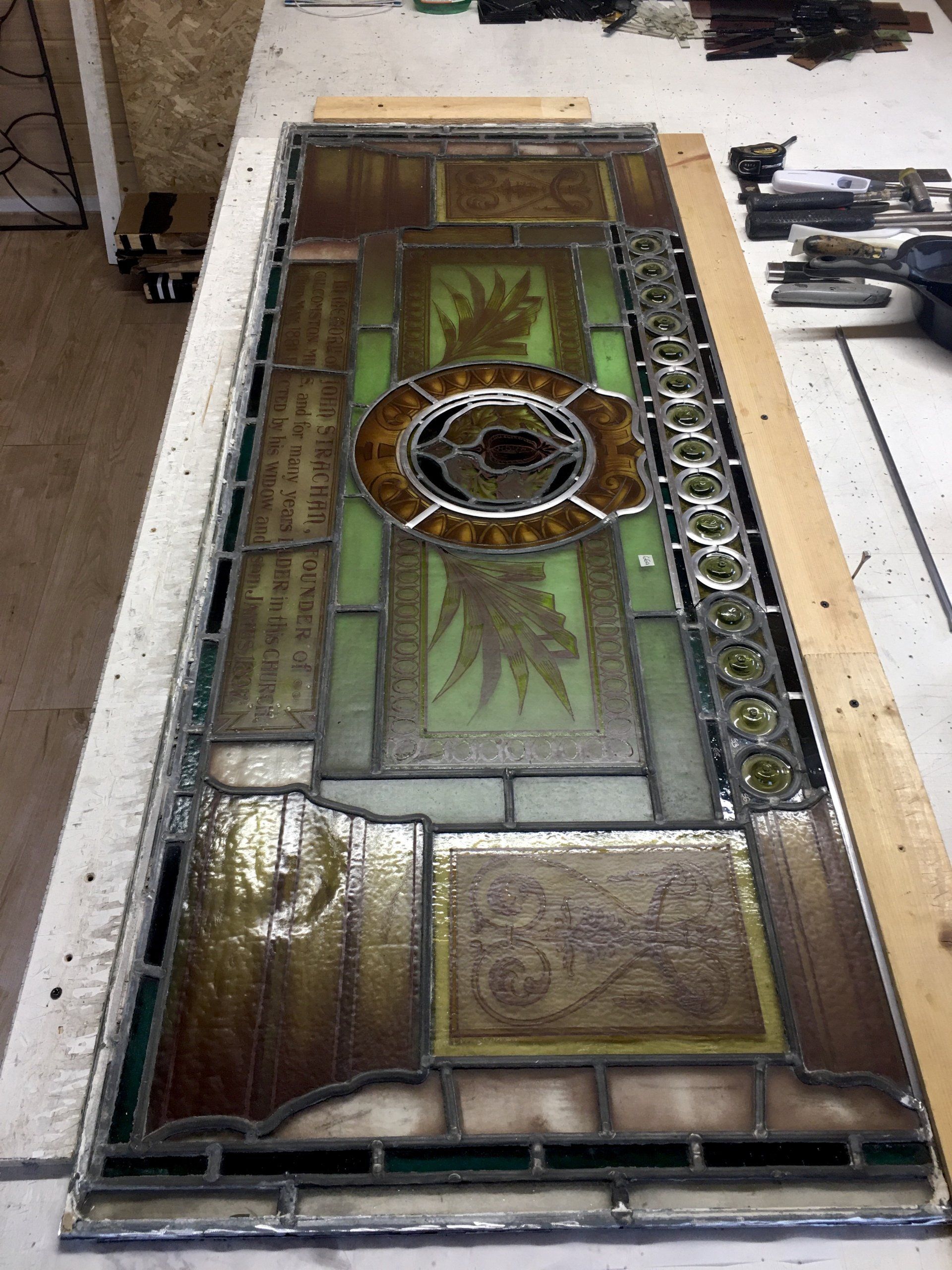 Wooden stained-glass door panel with a circular medallion, laid flat on a workshop floor.