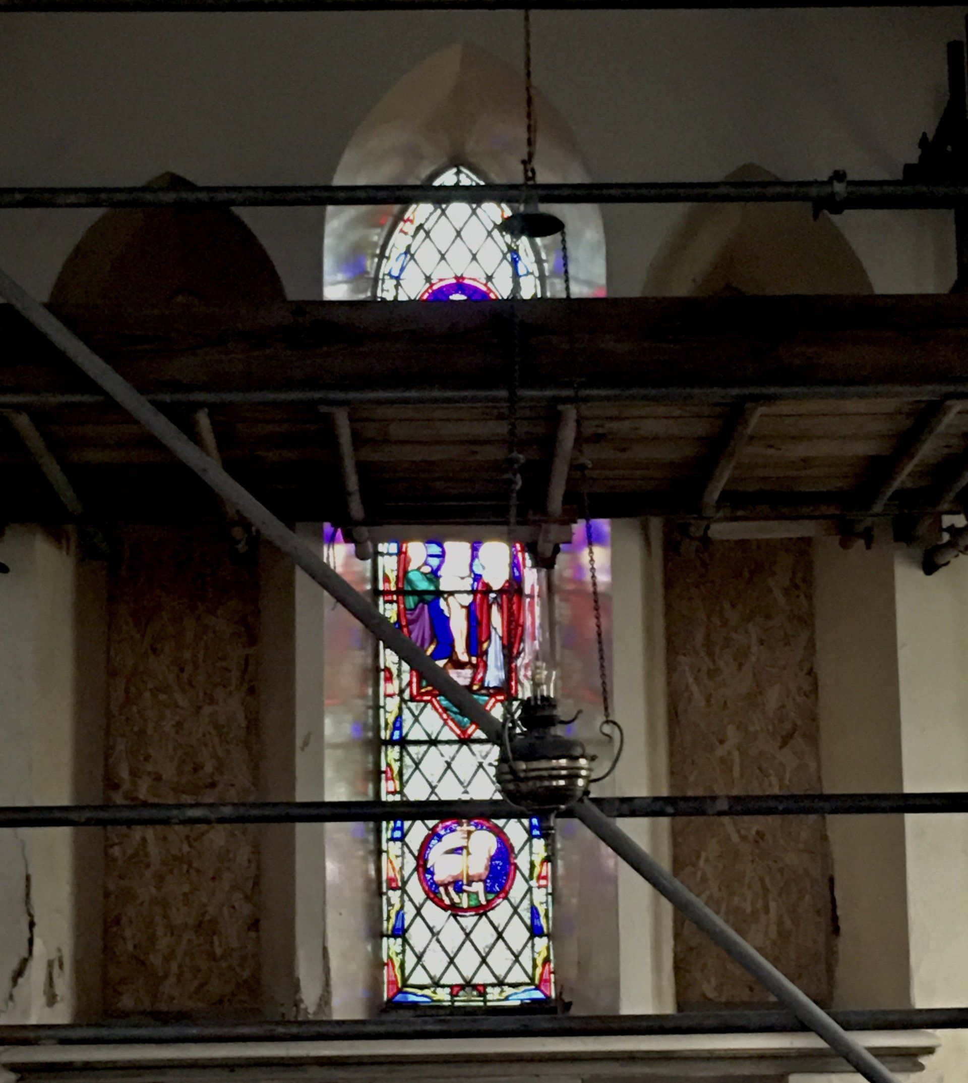 Stained glass window in a church, partly obscured by scaffolding and wooden beams.