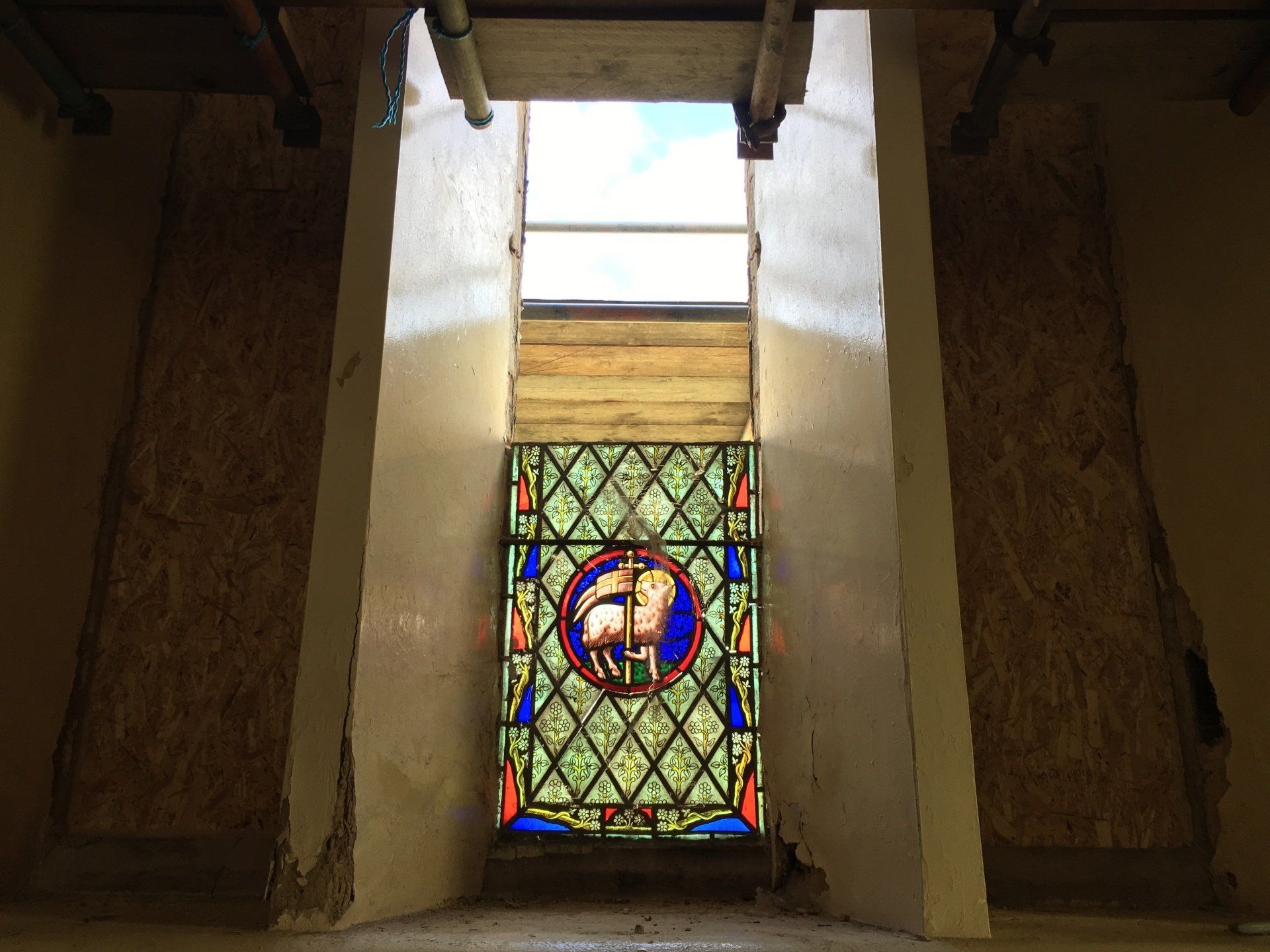 Stained-glass window in a narrow stone corridor, lit by daylight.