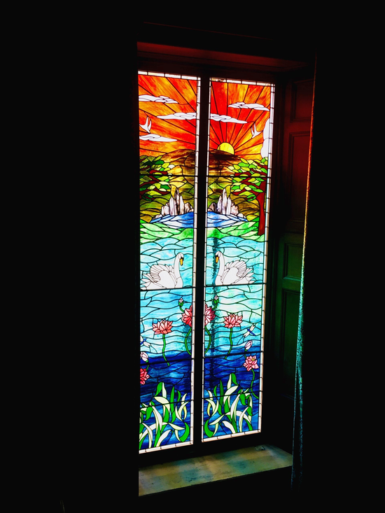 Tall stained-glass window with a vivid sunset, rainbow sky, and blue water scene