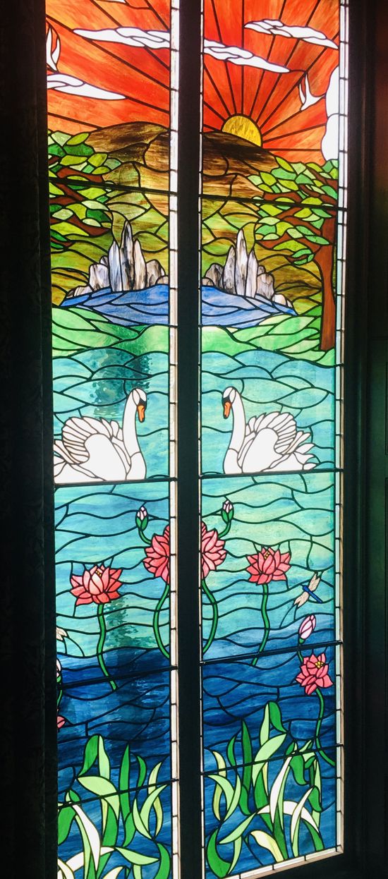 Colorful stained-glass panels showing a sunlit lake with swans, flowers, and a mountain landscape