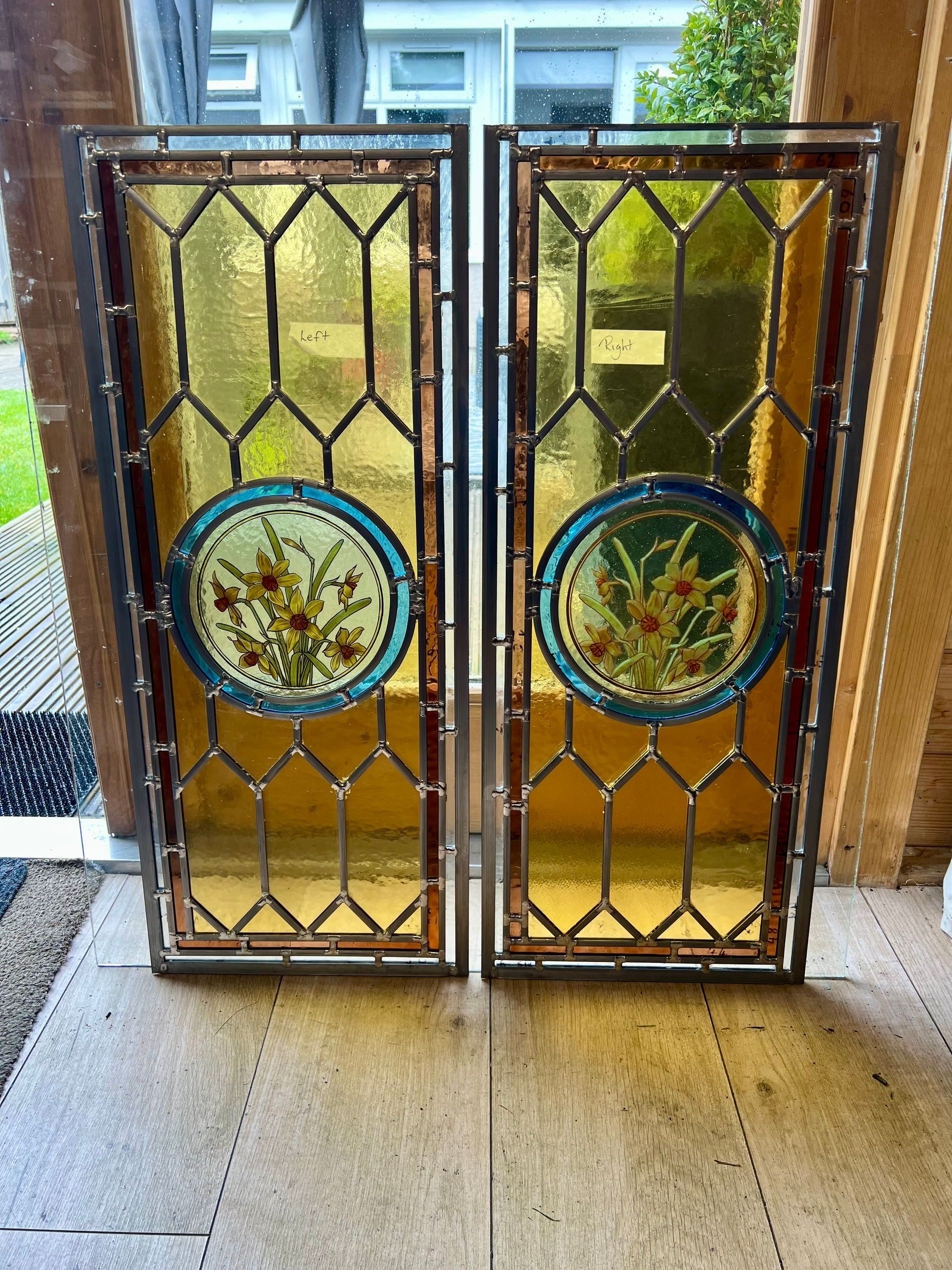 Two stained-glass door panels with circular floral medallions, leaning upright in a doorway.