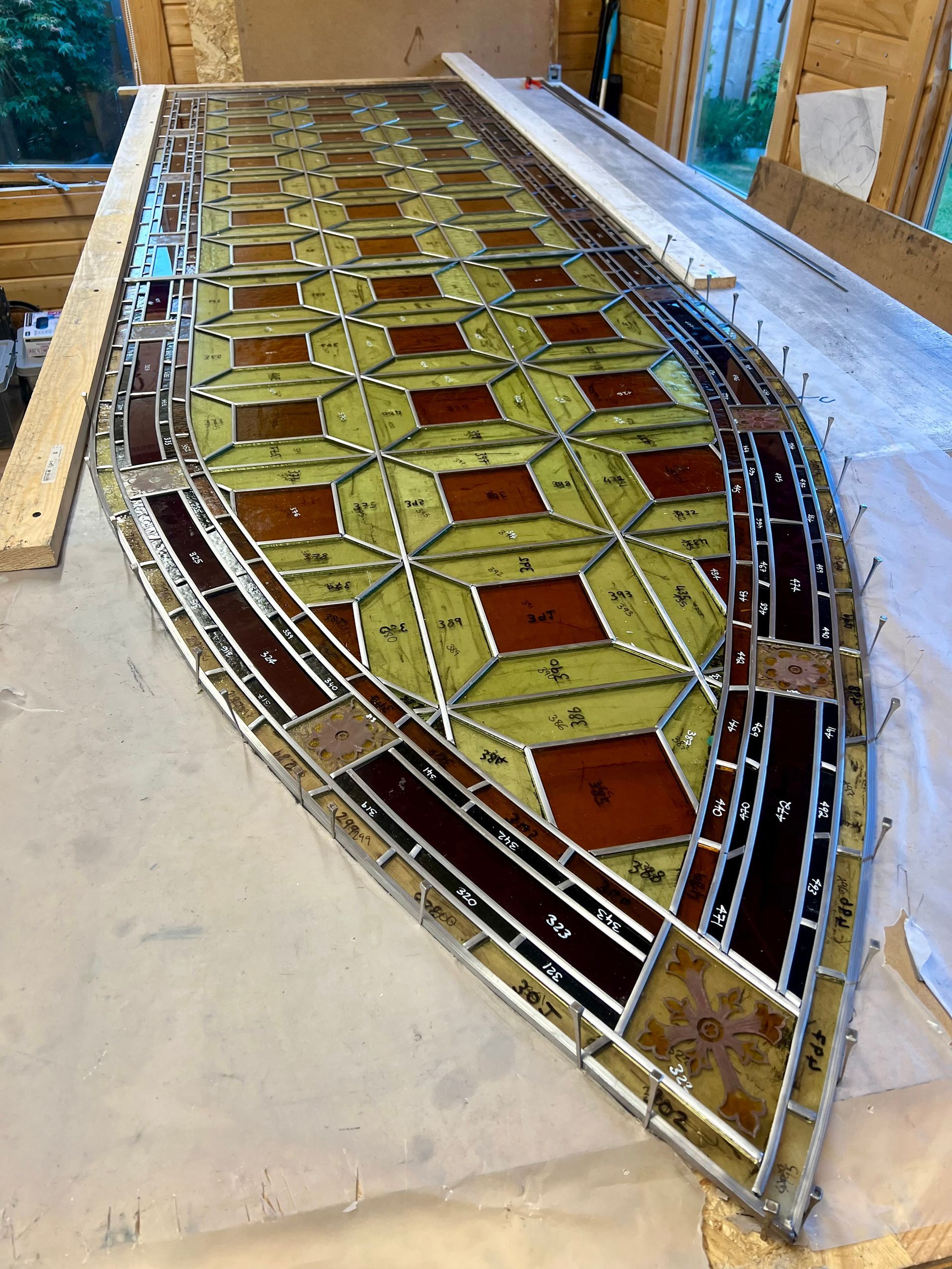 Curved stained-glass window panel with geometric yellow and red panes, lying on a workbench in a workshop