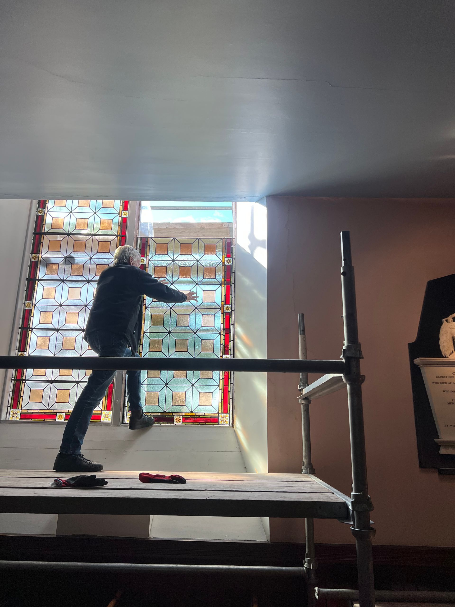 Worker on scaffolding installing or adjusting a backlit wall display inside a dark room