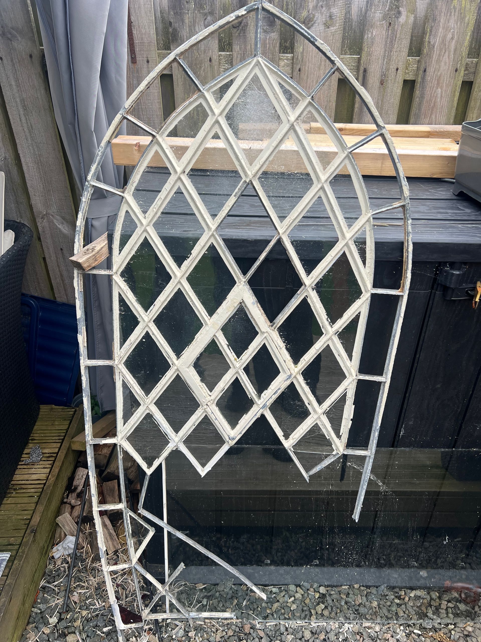 Arched white lattice trellis leaning against a black fence outdoors