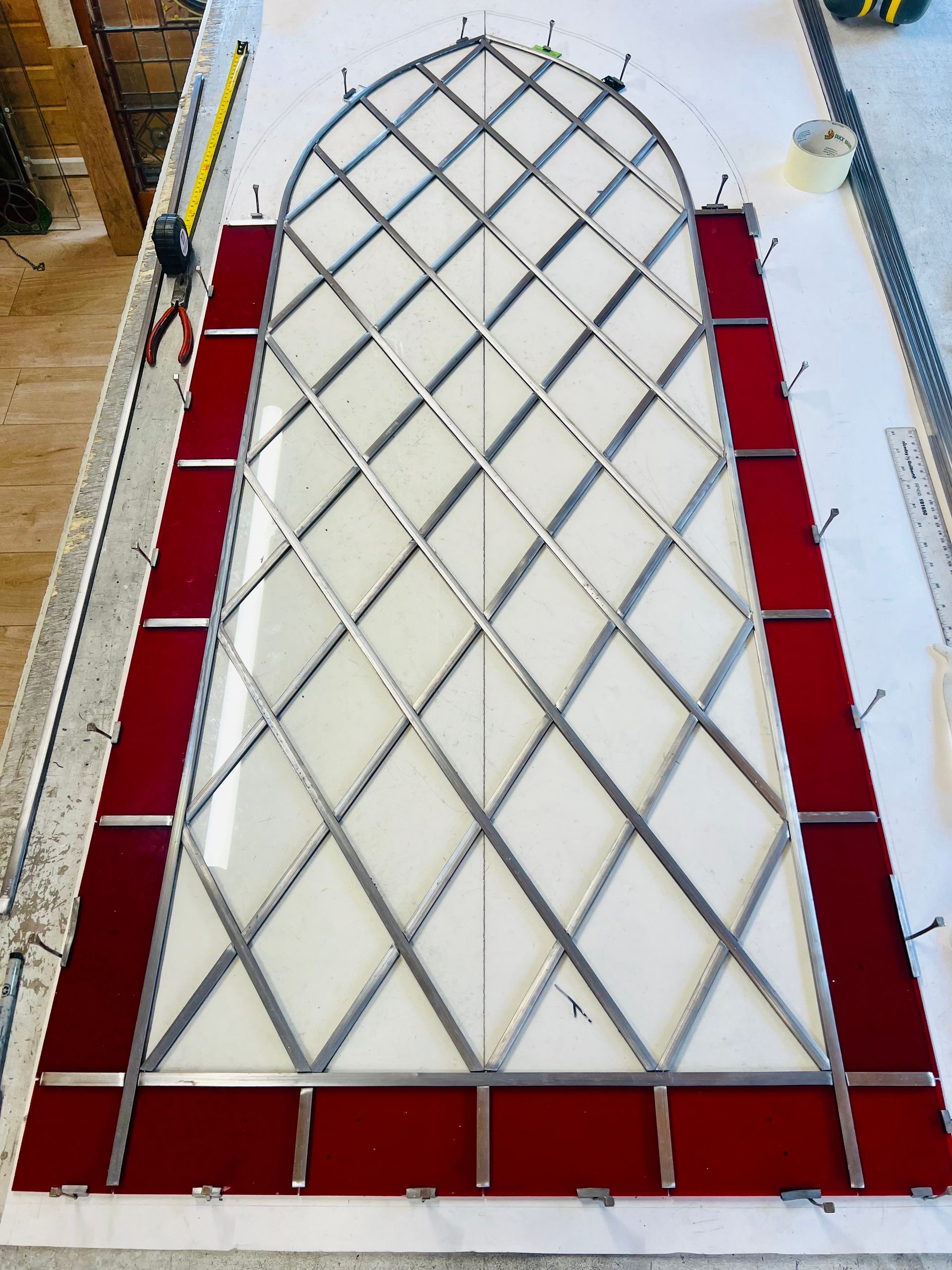 Tall arched lattice structure with red side and base panels, viewed from above on a workshop floor.
