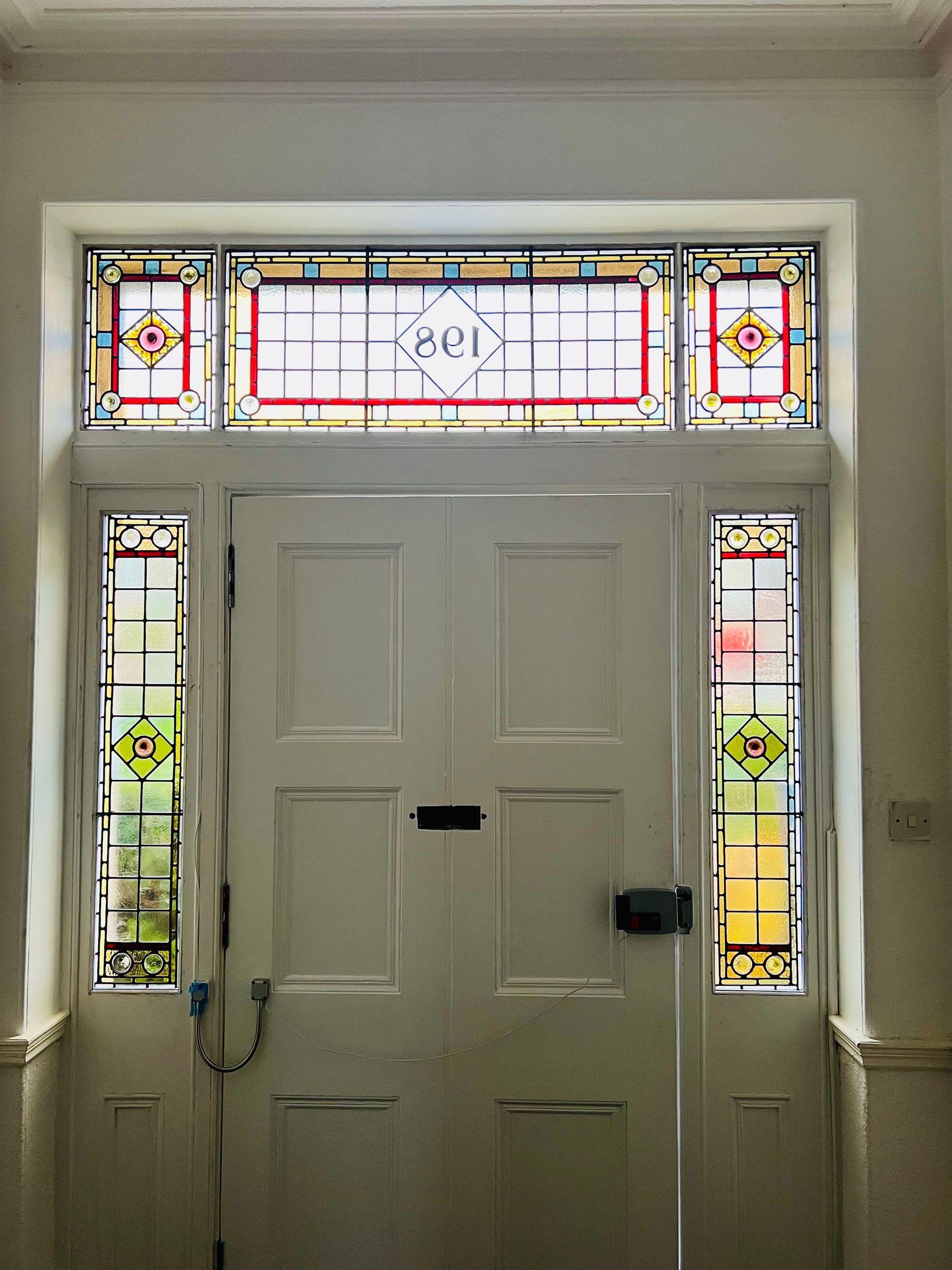 Front door with stained-glass side panels and transom window, viewed from inside a hallway