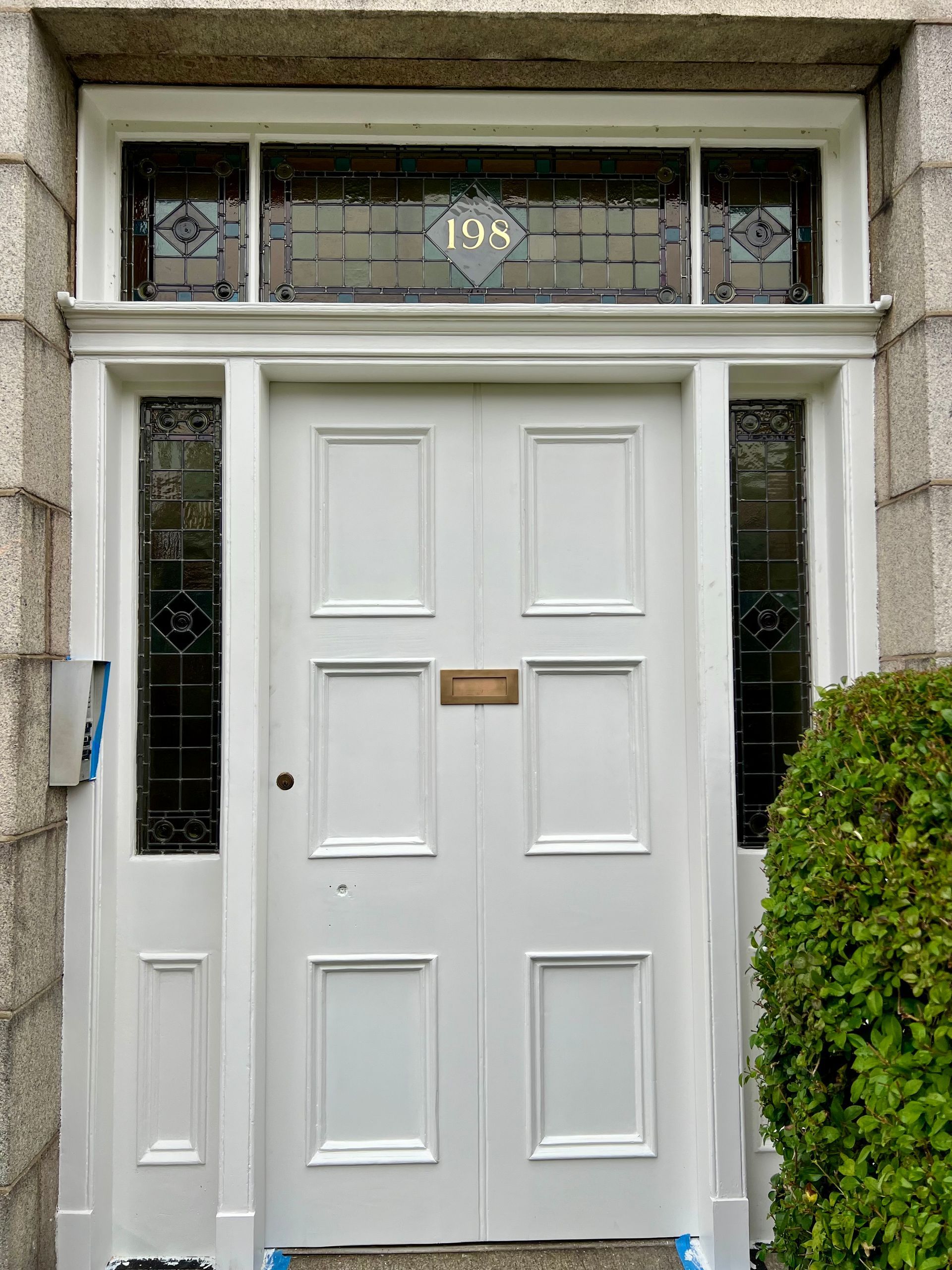 White front door with narrow glass sidelights and a transom window, set in a stone entryway.