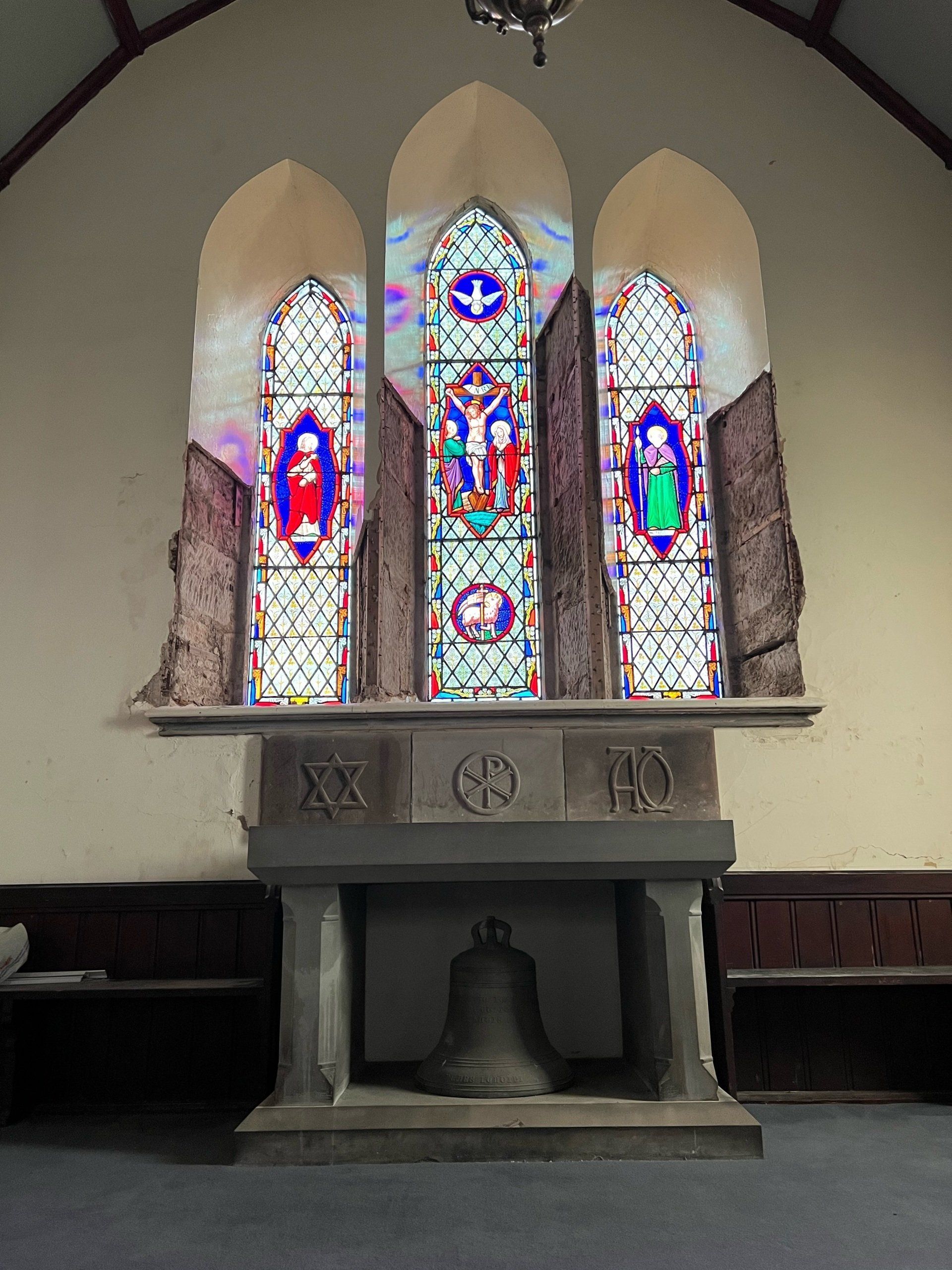 Stained-glass window above a stone altar in a church, with colorful religious figures and patterns.