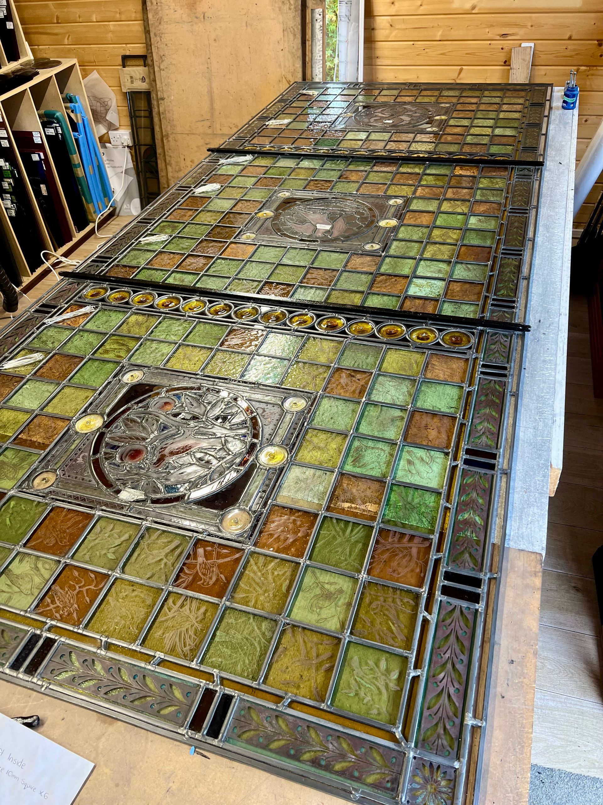 Stained-glass mosaic tabletop with green and amber tiles in a workshop, viewed from above