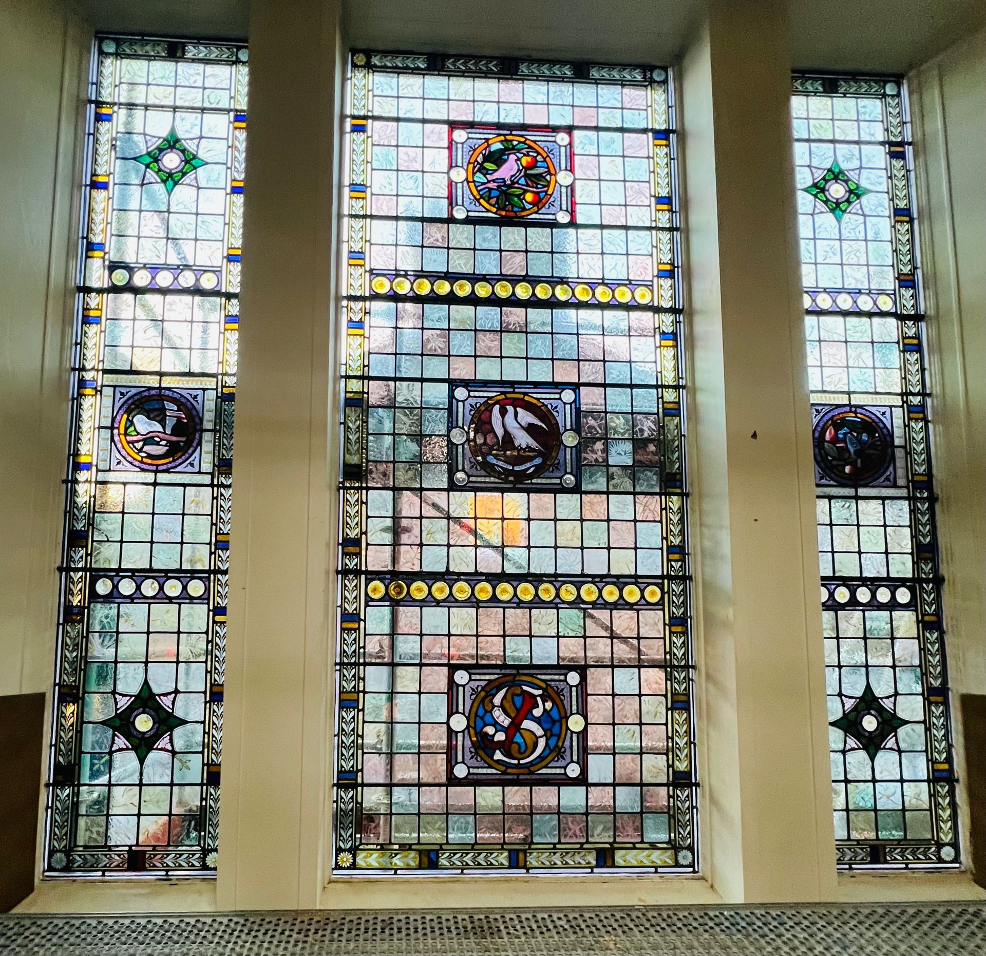 Three-panel stained glass window with geometric and circular multicolored designs