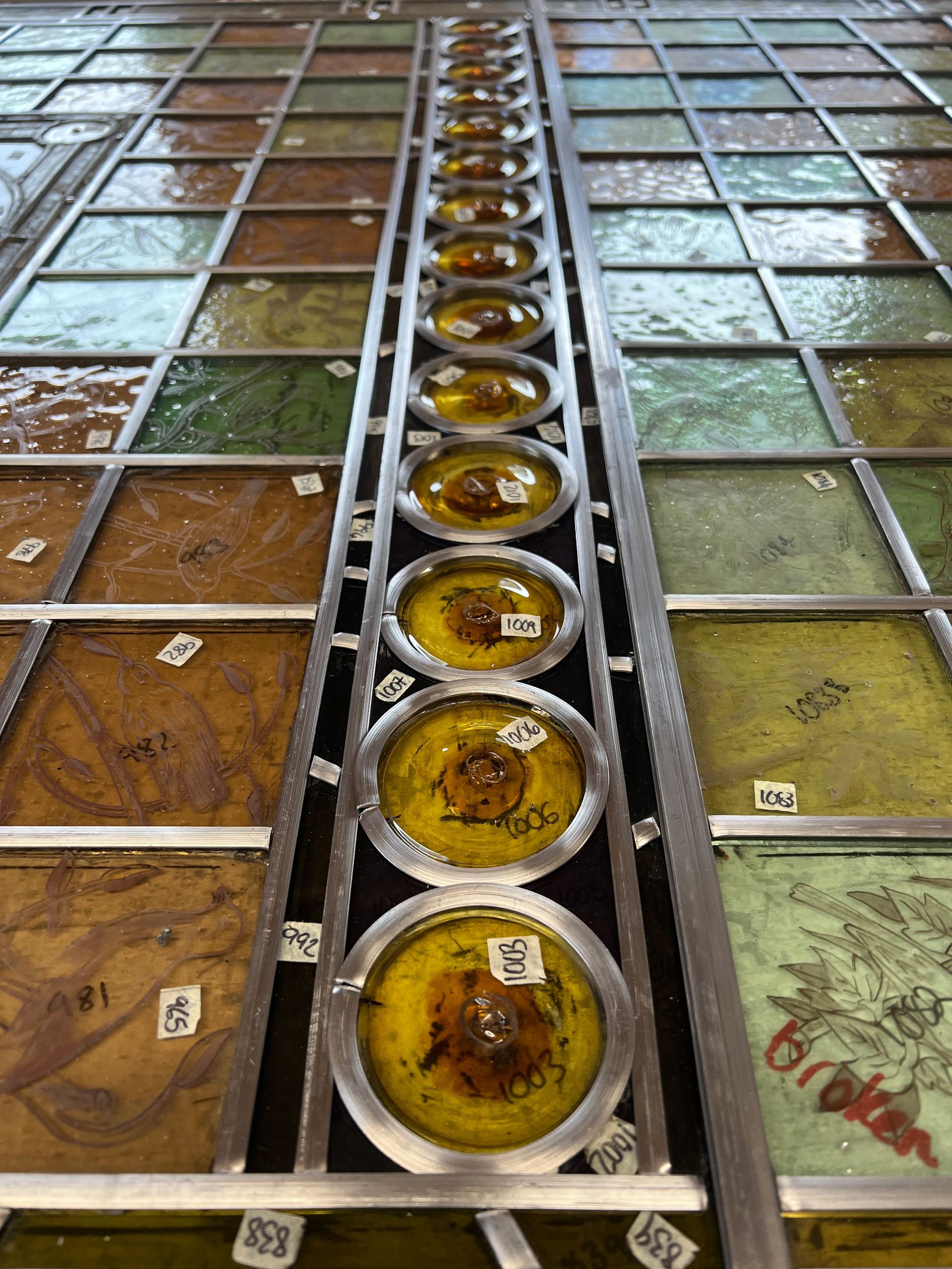 Rows of stained glass panels with a central line of round yellow bowls in a workshop-like setting