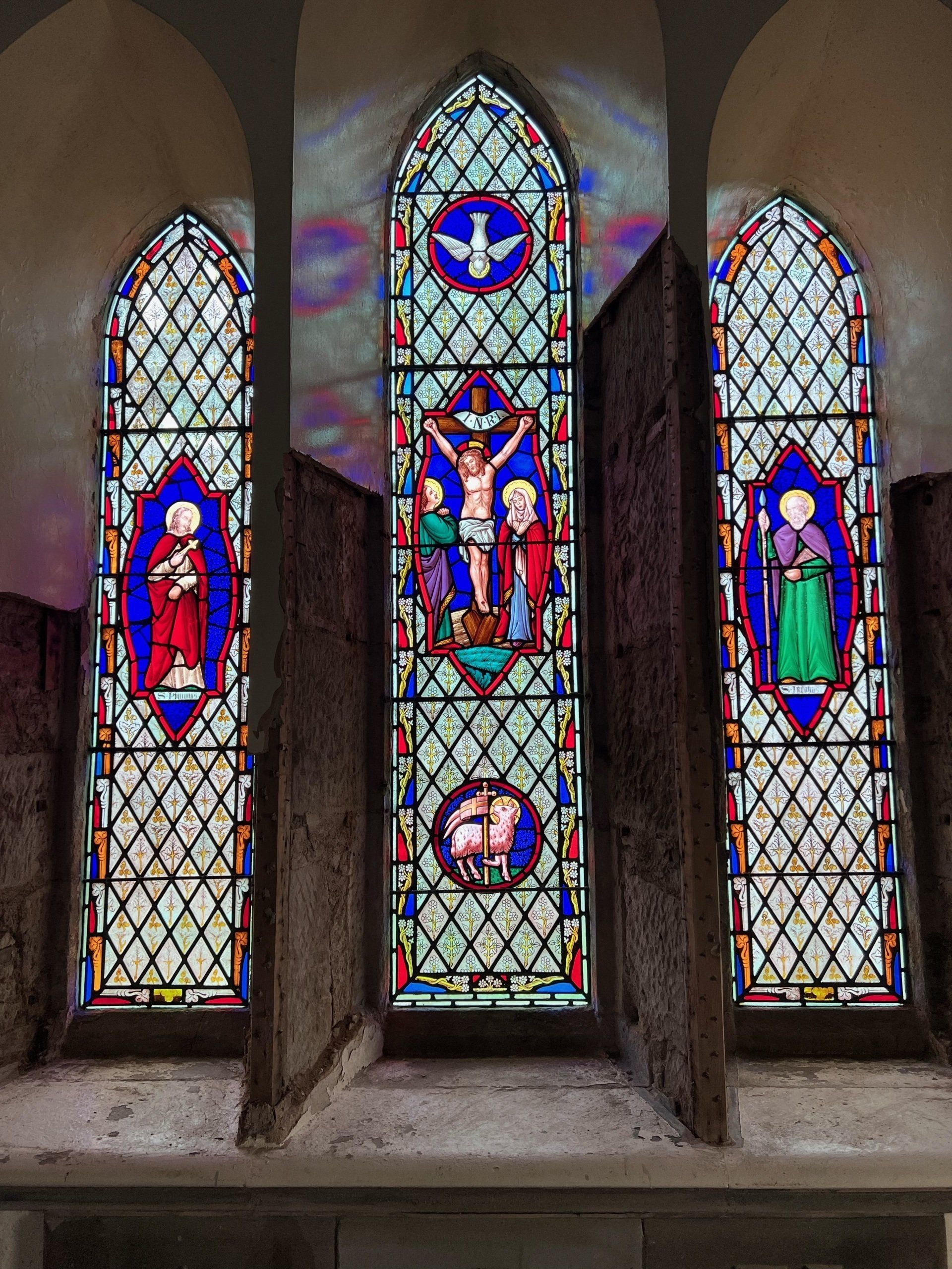 Three stained-glass church windows with religious figures and colorful geometric patterns