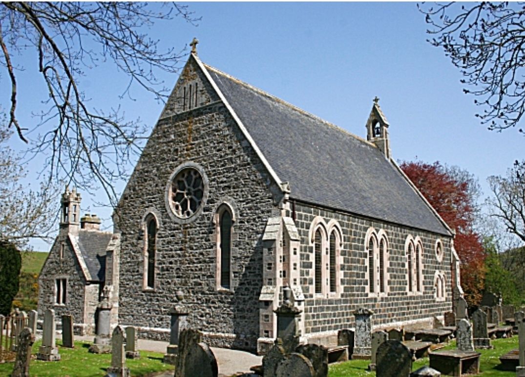 Stone church with gray slate roof and stained-glass windows in a cemetery on a sunny day