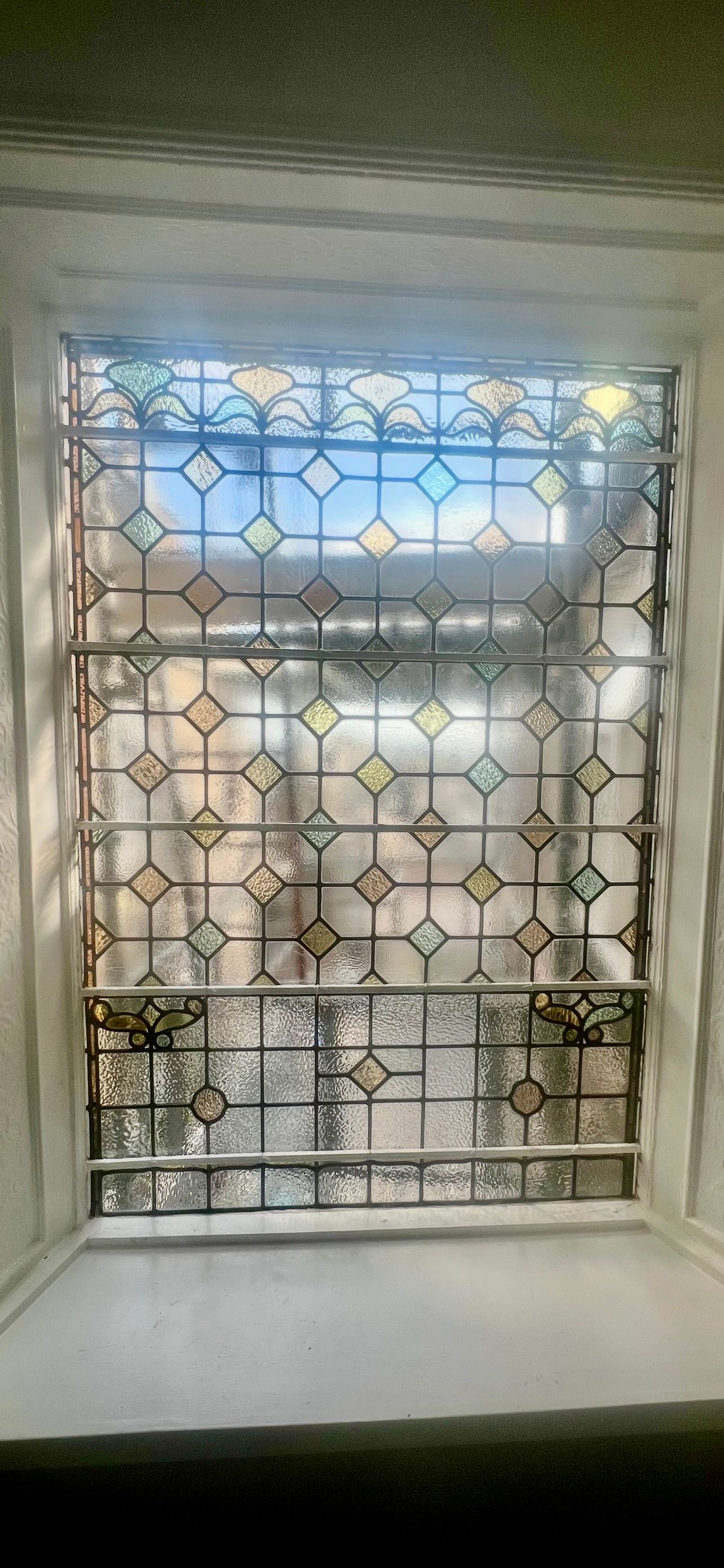 Sunlit window with ornate metal grille, looking out onto a balcony and blue sky