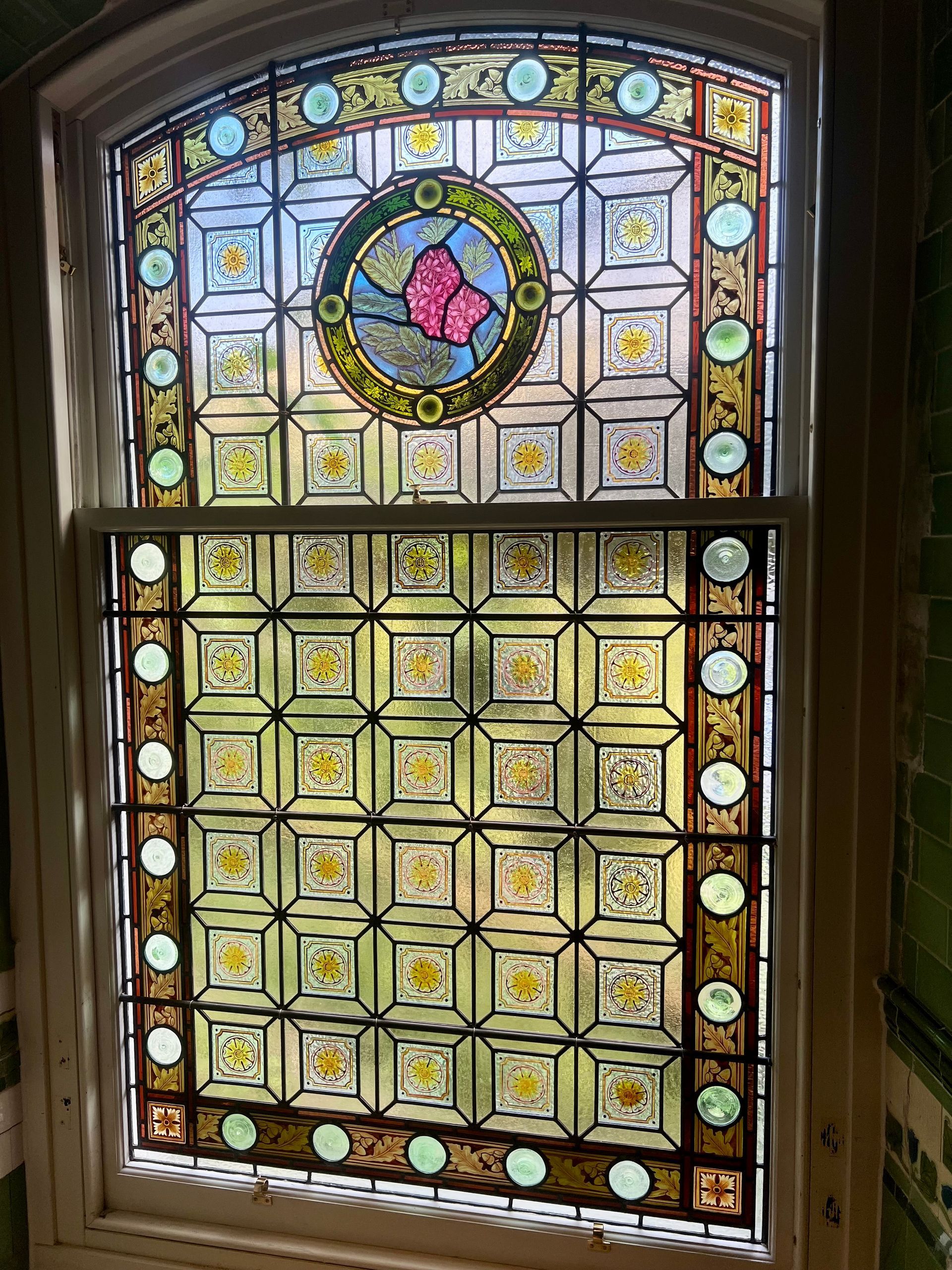 Decorative stained-glass window with circular floral medallion and pale yellow panes in a wooden frame