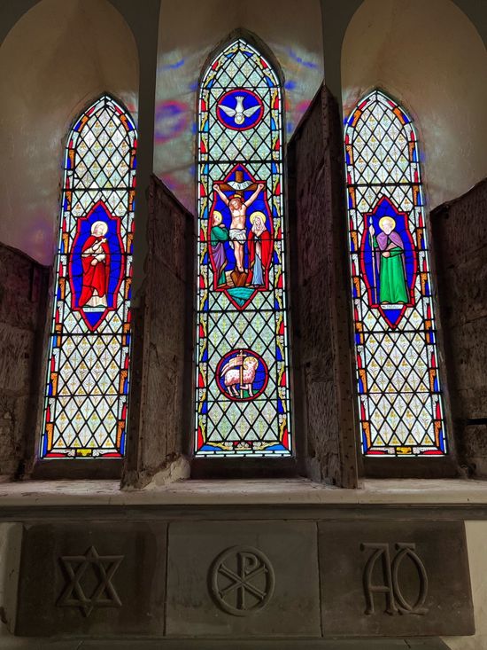 Three stained-glass church windows with colorful religious figures above carved symbols