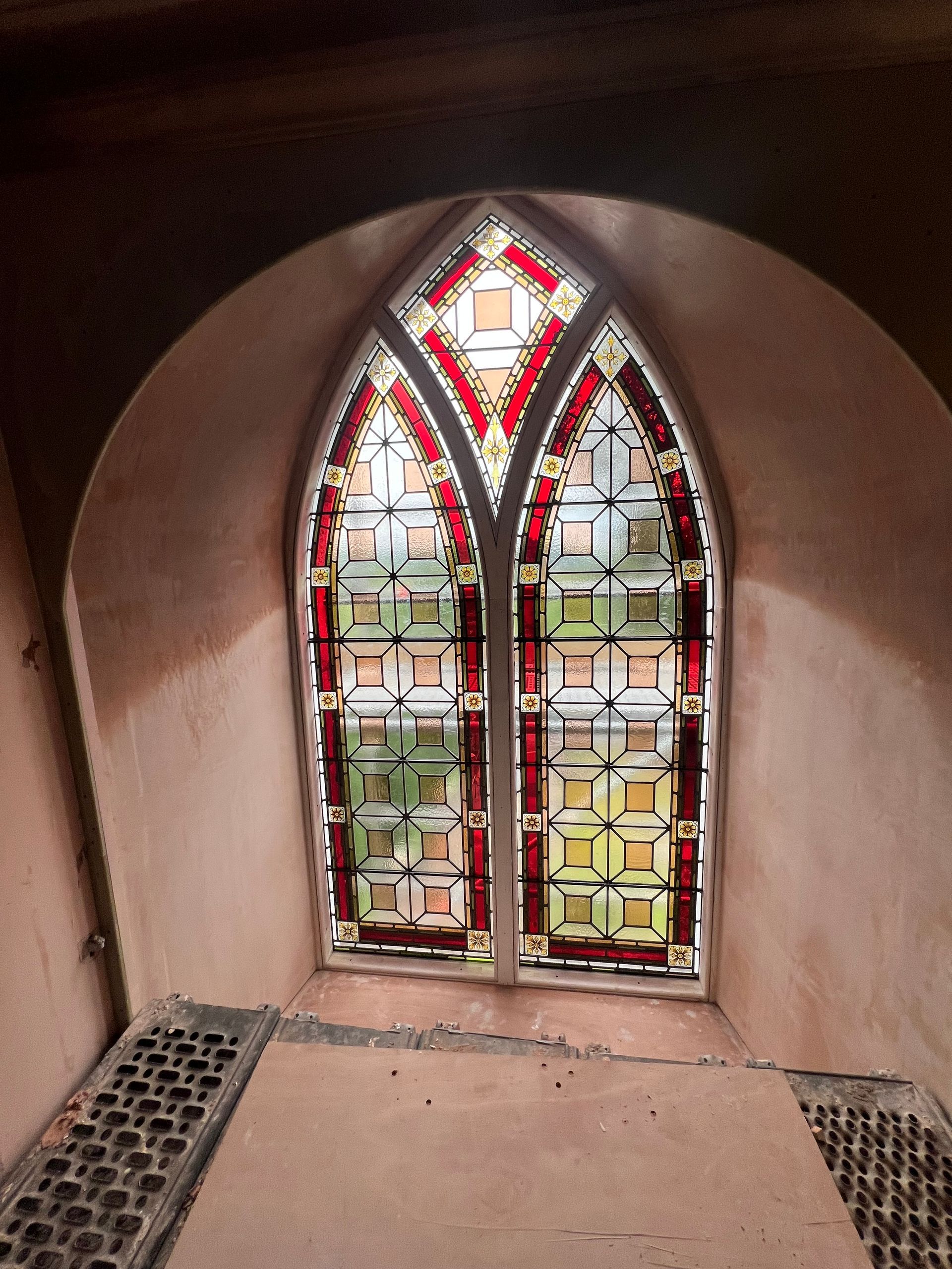 Decorative stained-glass window in a rounded alcove with pink plaster walls and tiled ledges